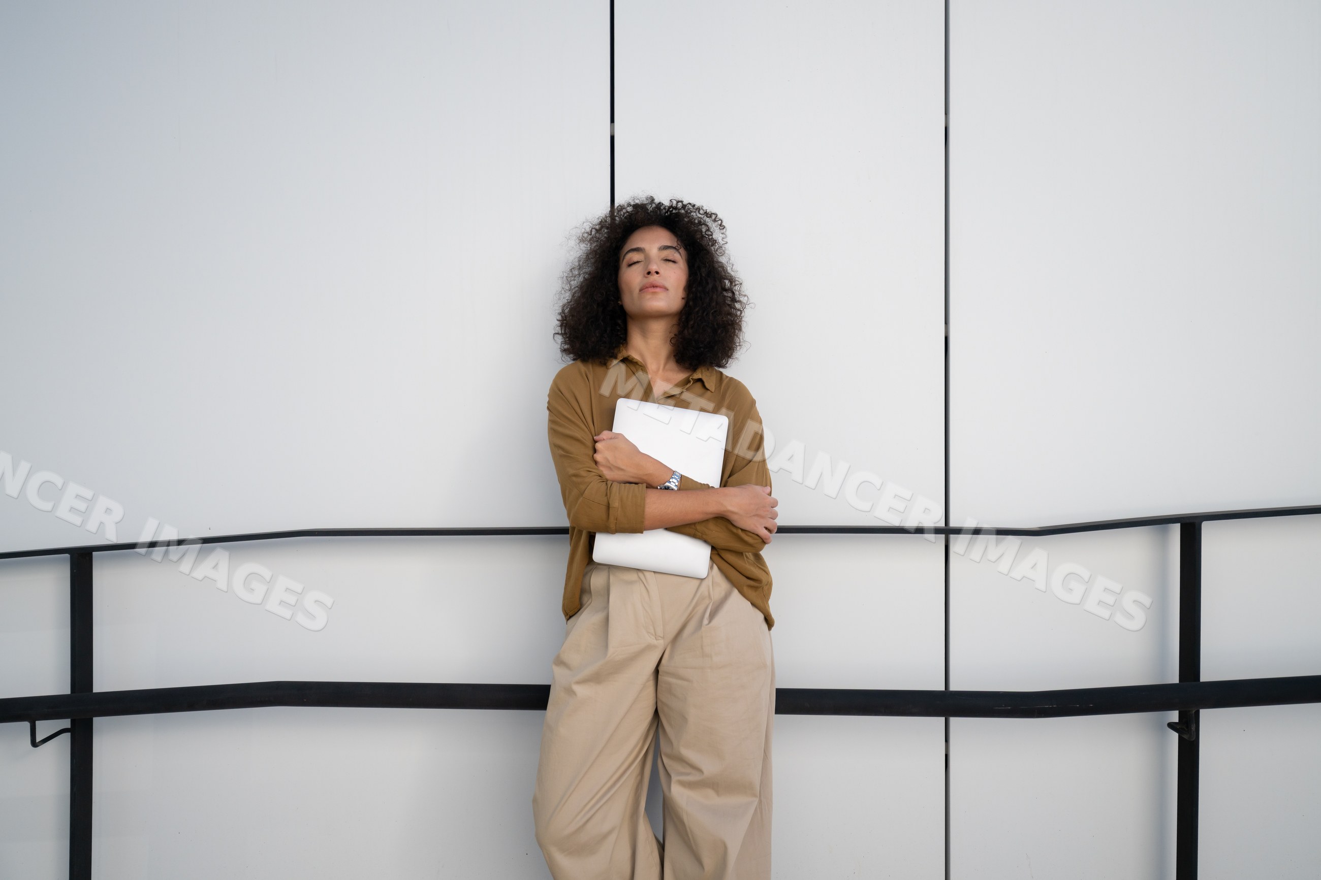 Woman holding laptop with closed eyes against white wall