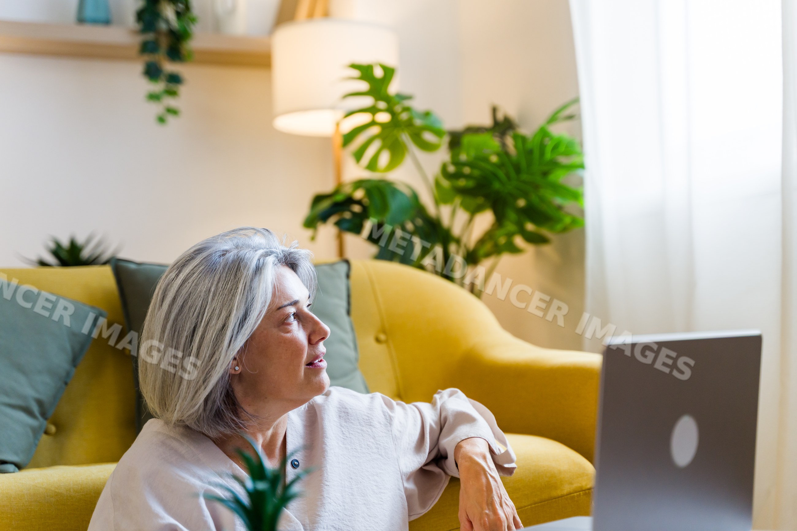 White woman sitting on floor by yellow sofa and laptop