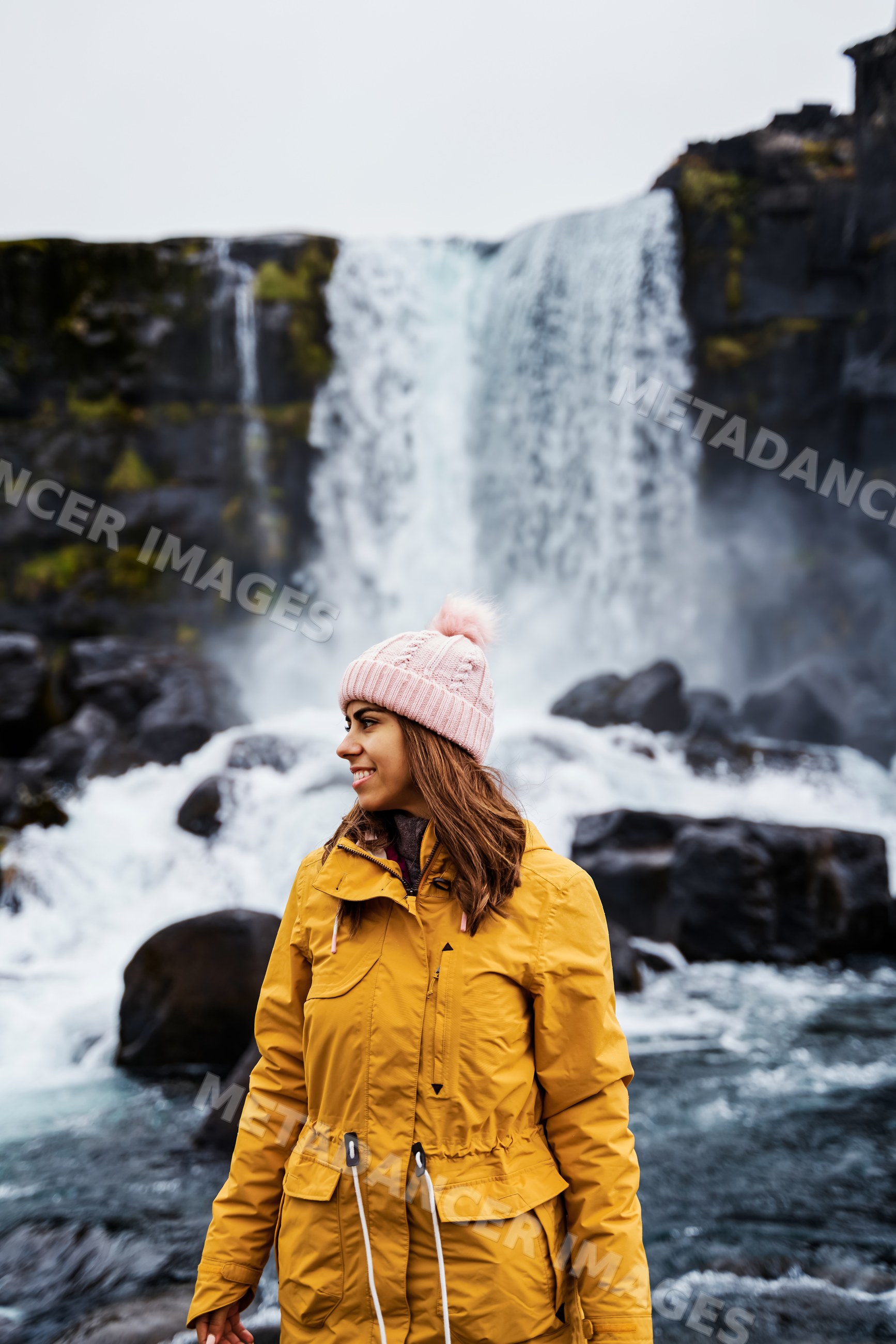 A white woman in a yellow jacket enjoys the scenery near a waterfall