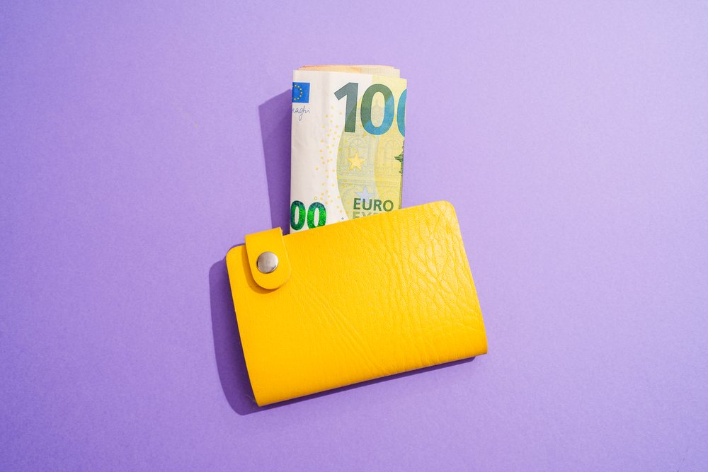Yellow wallet holding rolled 100 euro bill on purple background
