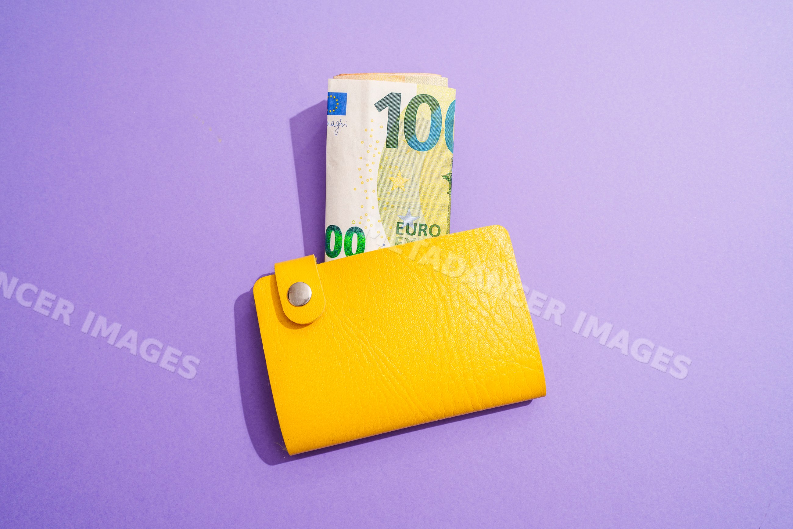 Yellow wallet holding rolled 100 euro bill on purple background