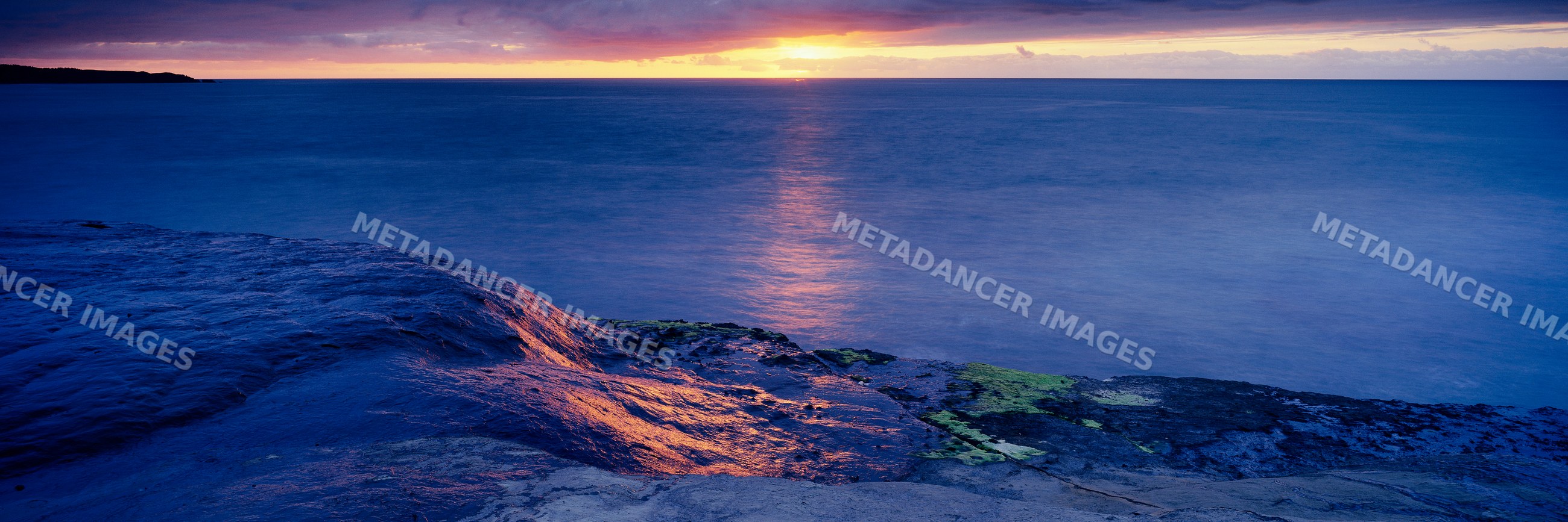 Sunset over rocky ocean shoreline with calm water