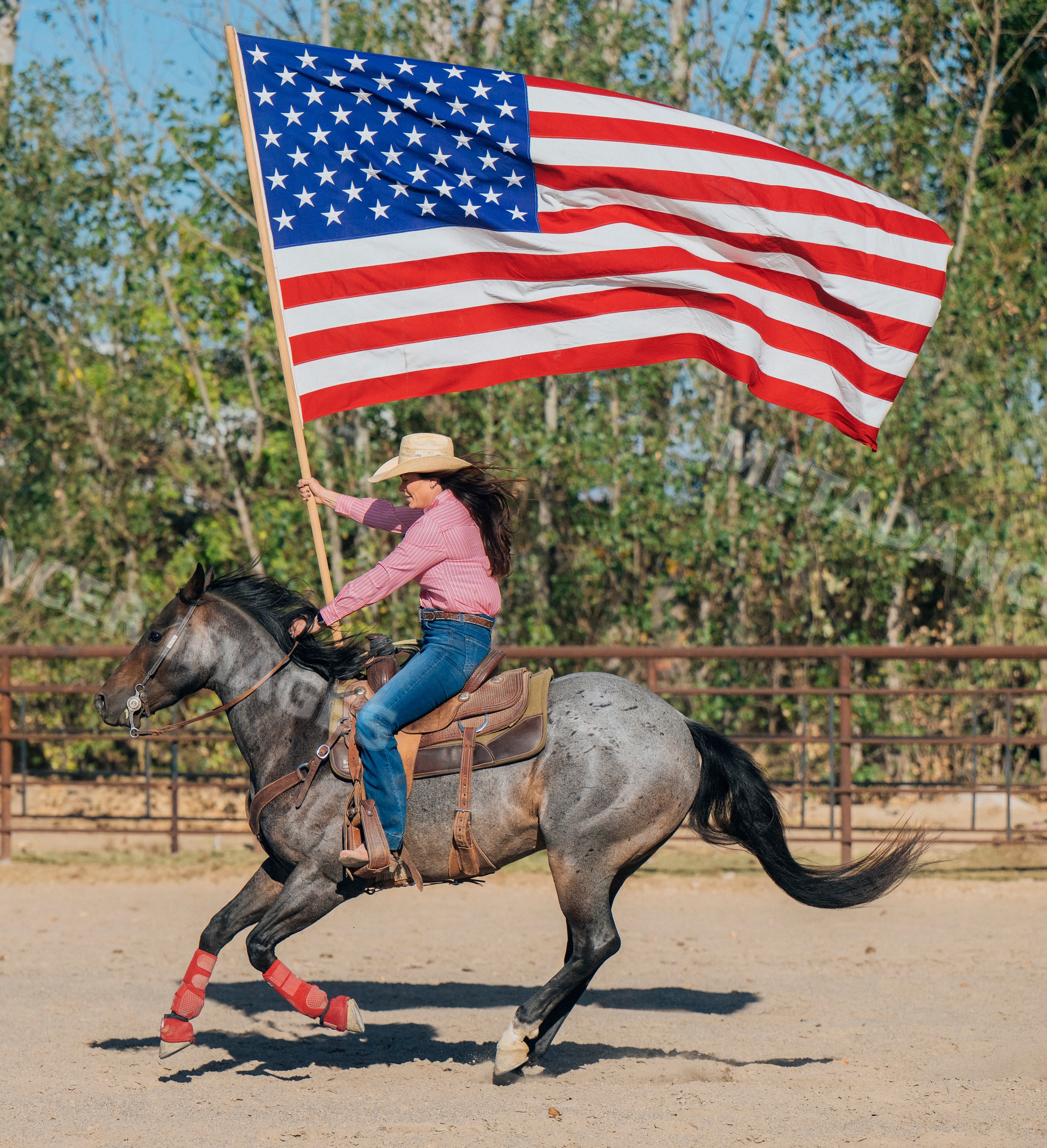 White person riding horse waving american flag in outdoor arena