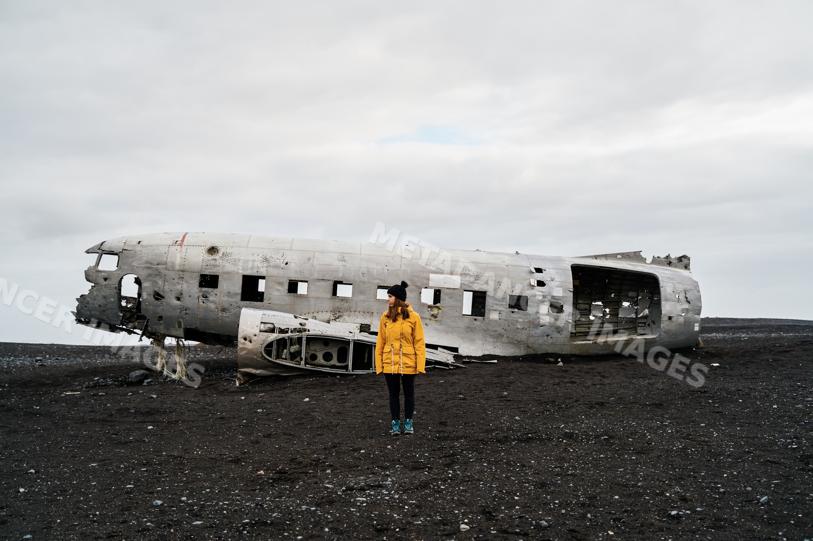 A white woman stands by crashed airplane wreckage on volcanic terrain