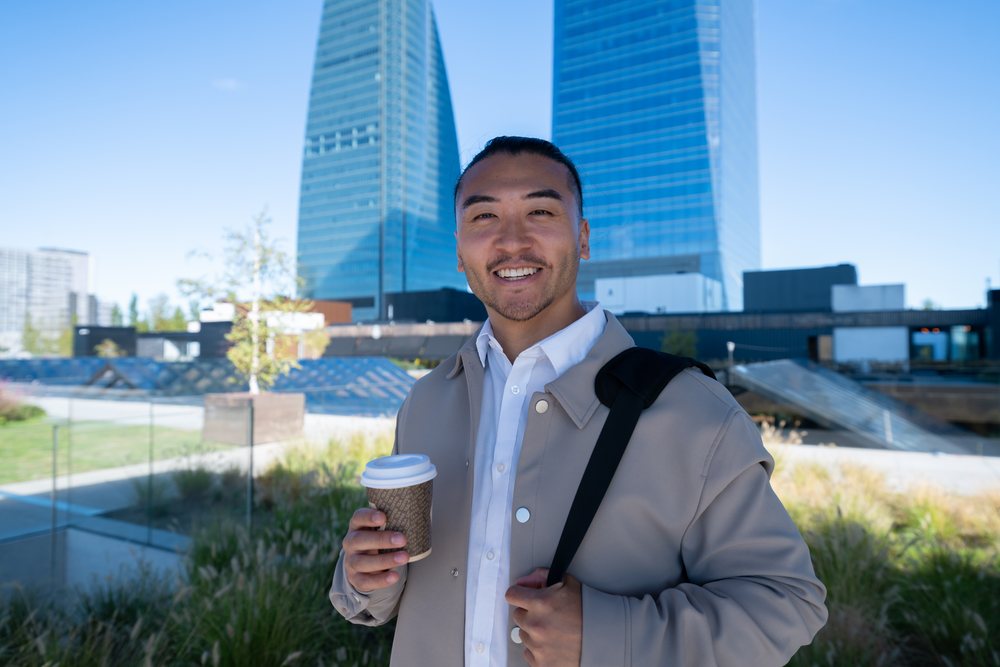 Man holding coffee cup outdoors near modern city buildings in Madrid
