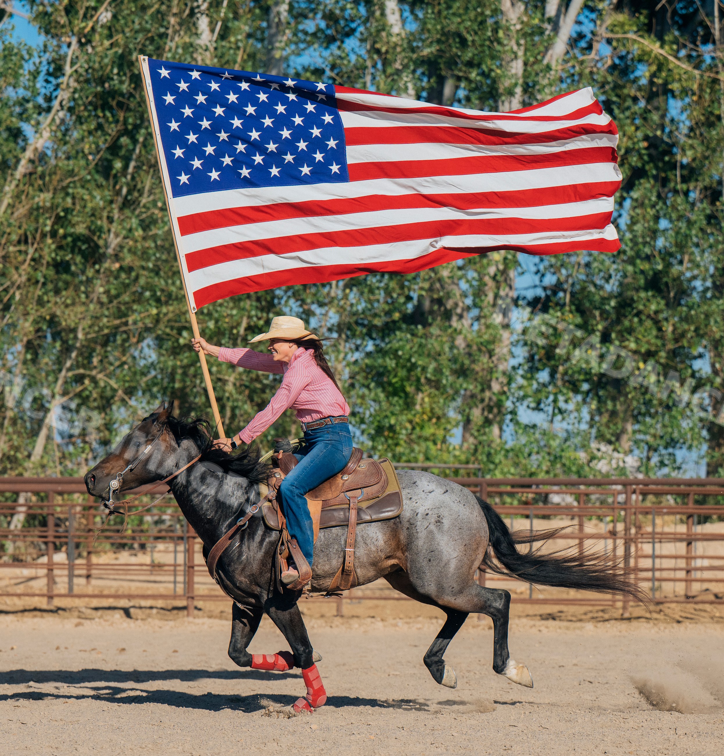 White woman riding horse while carrying american flag in outdoor arena