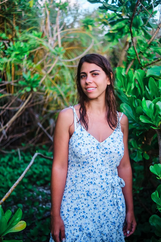 A young white woman smiles outdoors surrounded by tropical plants
