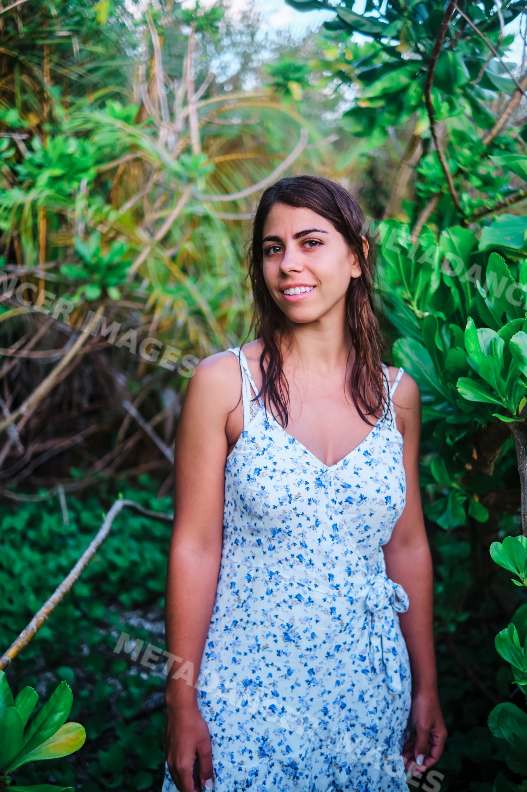 A young white woman smiles outdoors surrounded by tropical plants