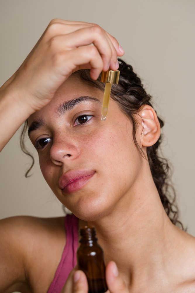 Hispanic woman applying face serum using dropper for skin care