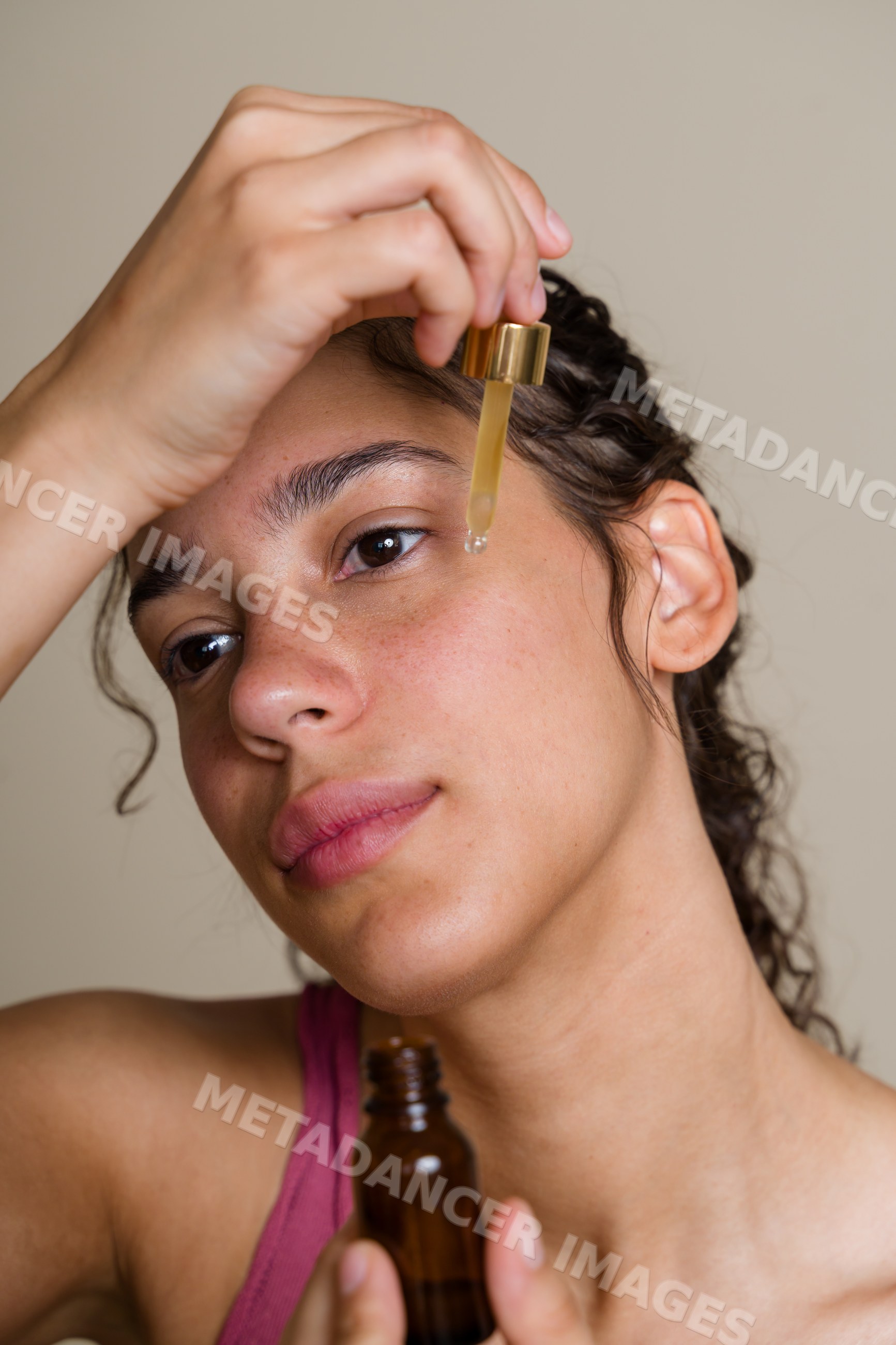 Hispanic woman applying face serum using dropper for skin care