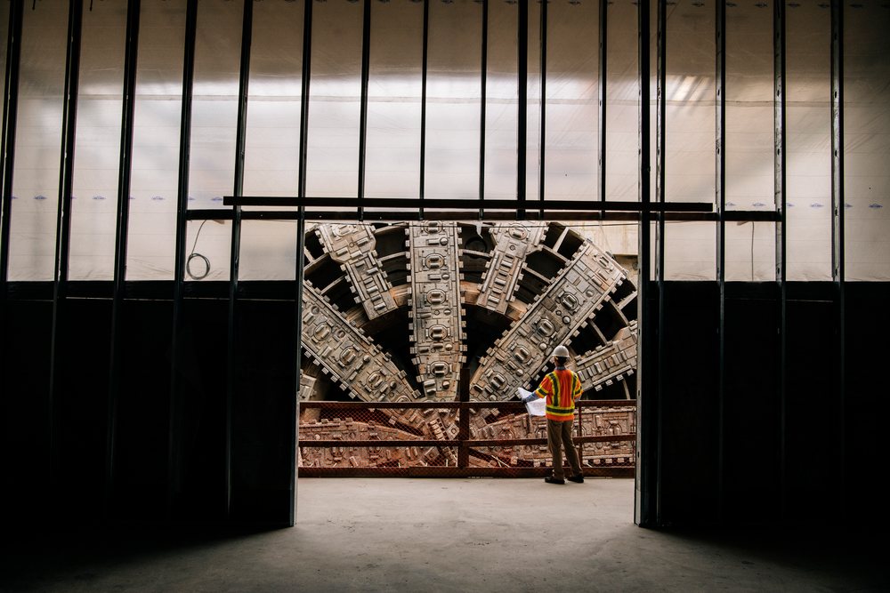 White construction worker inspects a large tunnel boring machine