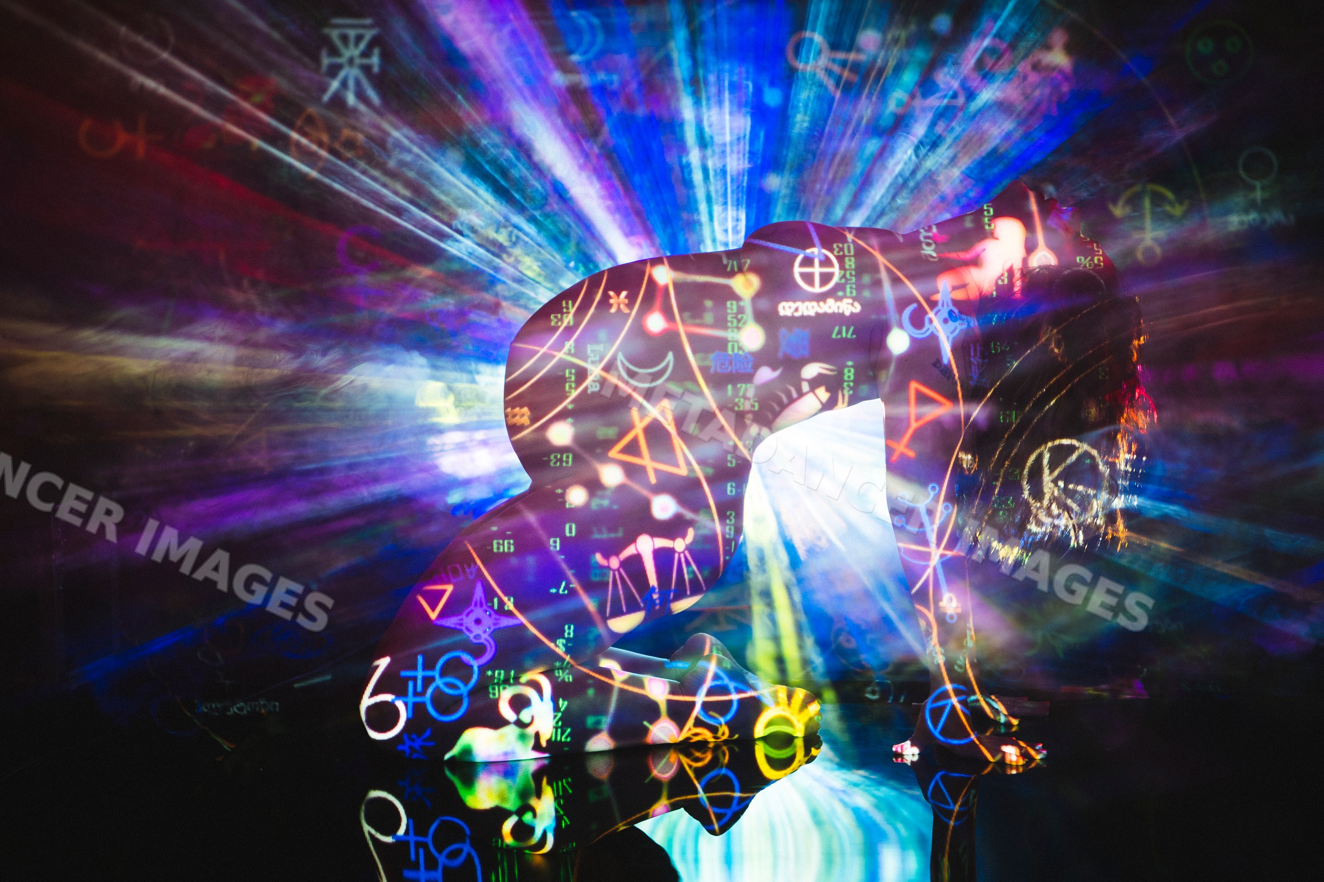 Nude white person kneeling with vibrant symbolic light projections