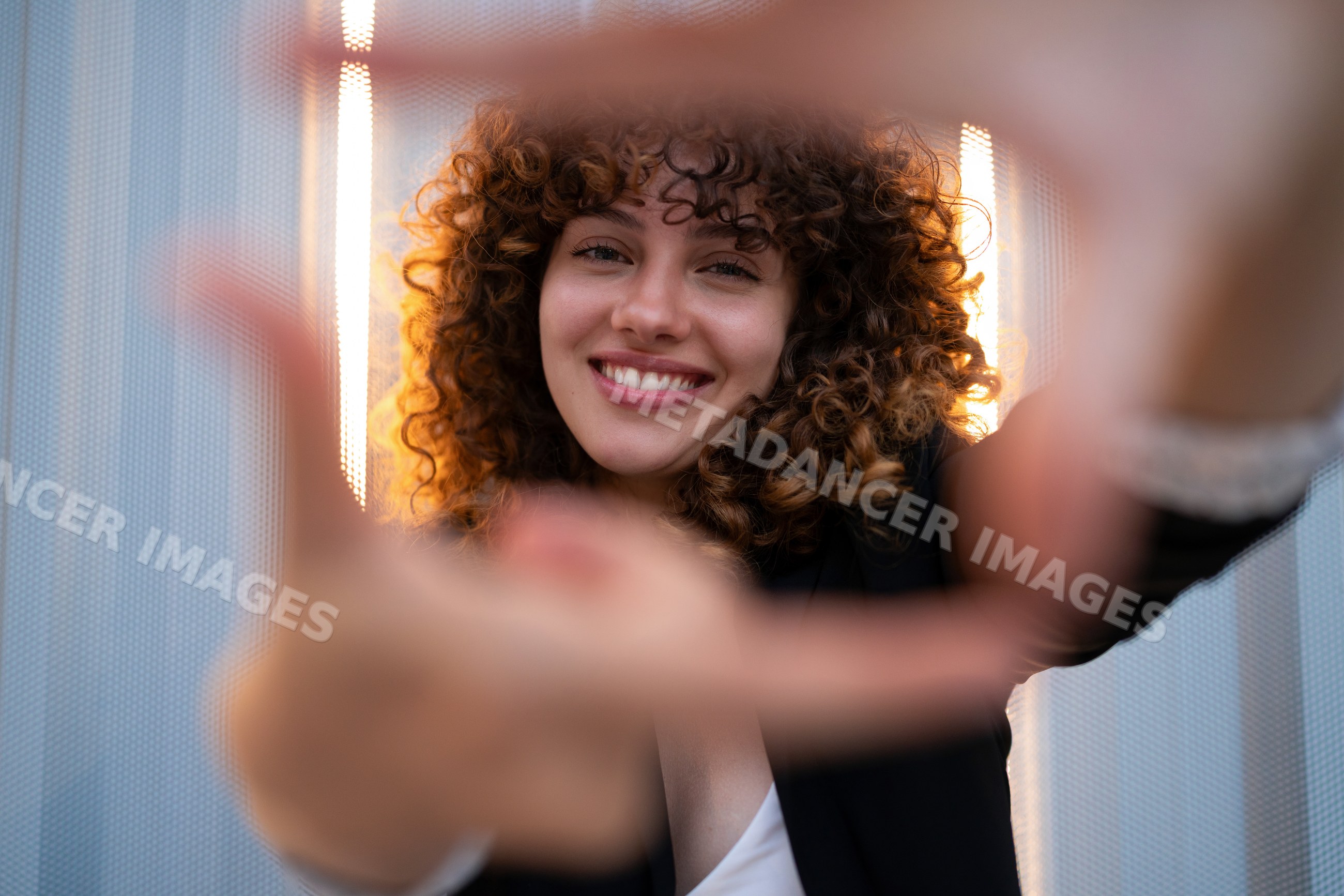 Smiling white woman with curly hair reaches toward camera