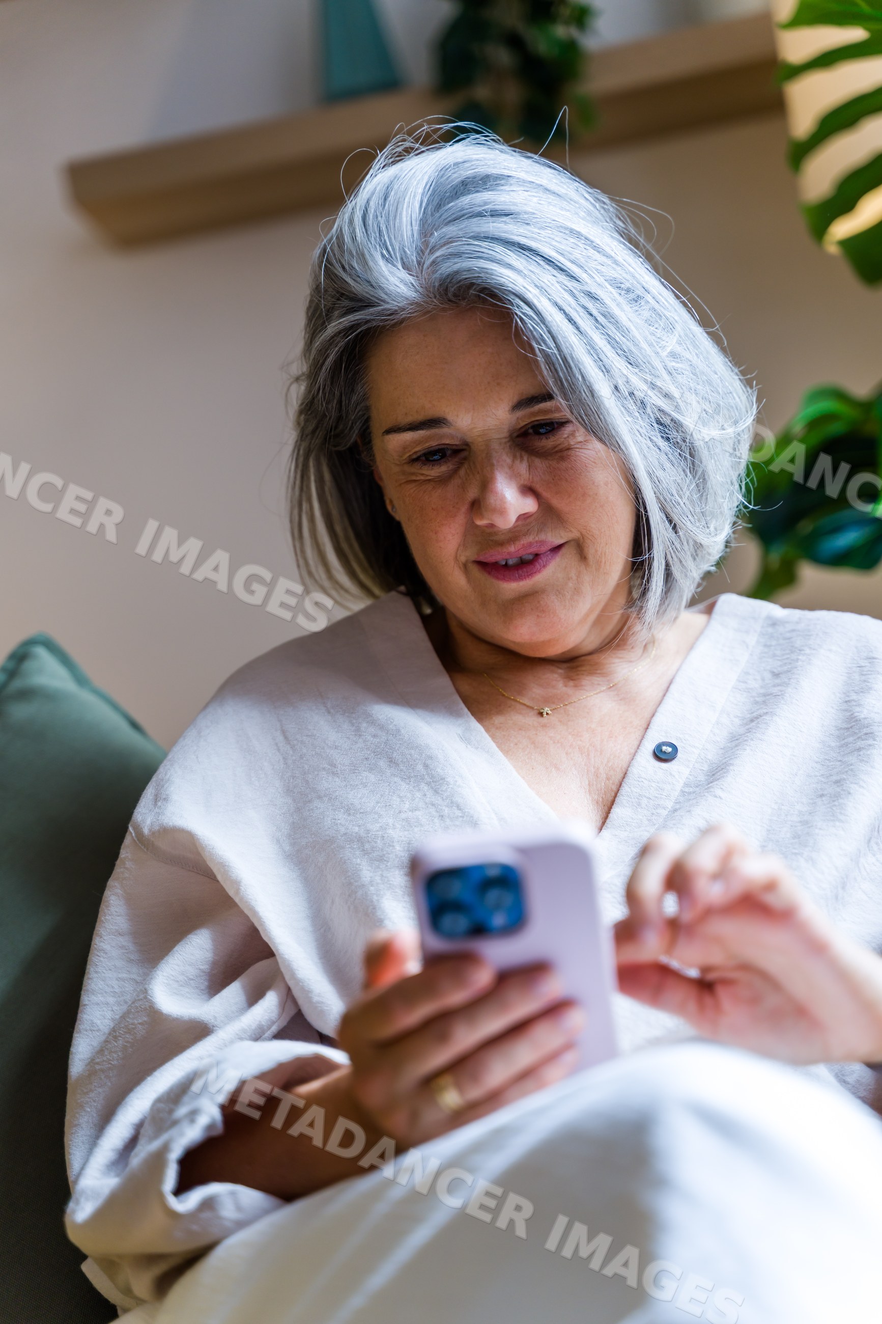 White woman with gray hair using smartphone on couch indoors