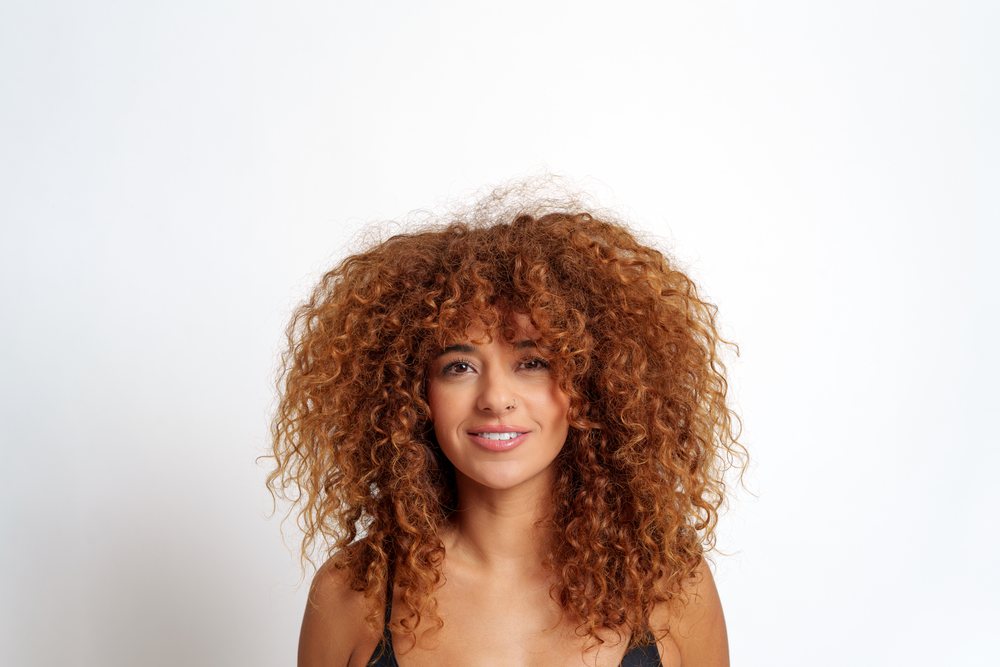 Hispanic woman with voluminous curly red hair smiling
