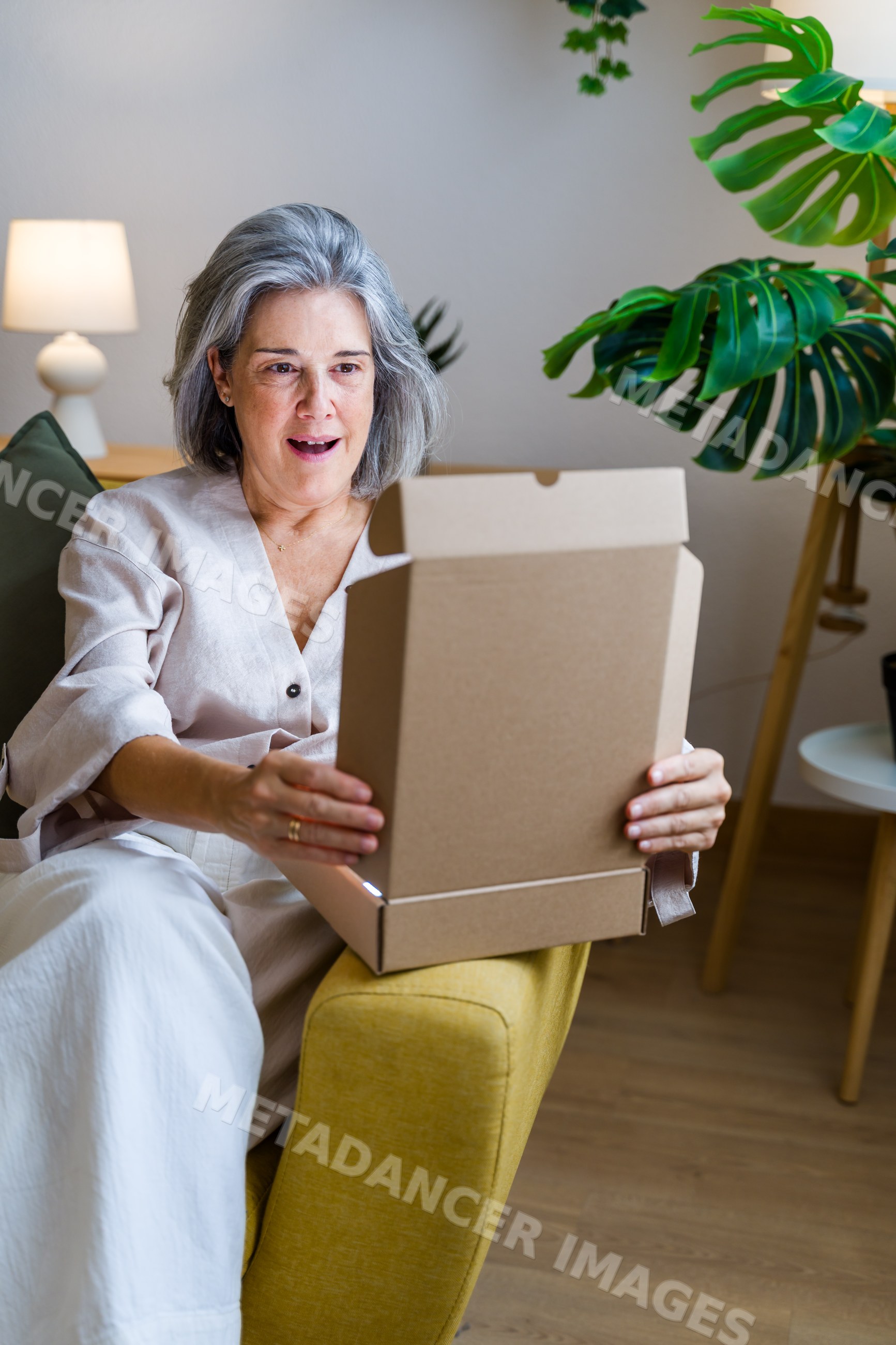 White woman opening cardboard box while sitting in yellow armchair