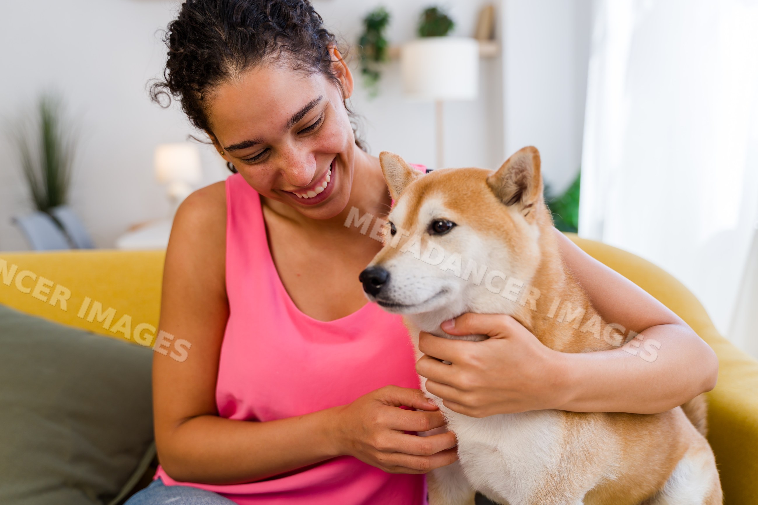 A Hispanic woman affectionately pets her dog in a cozy living room