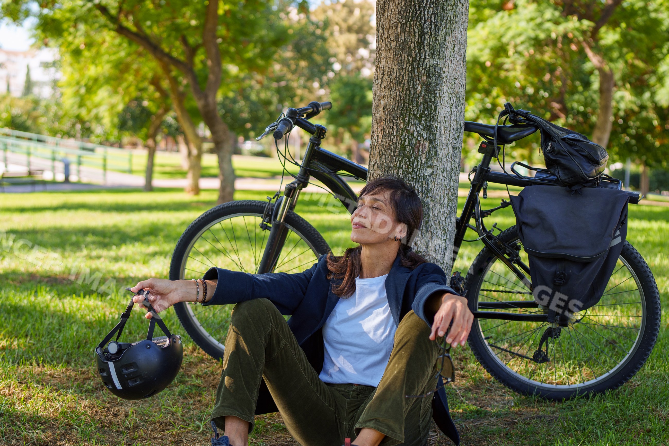 Hispanic woman resting under tree with bicycle in park in Málaga