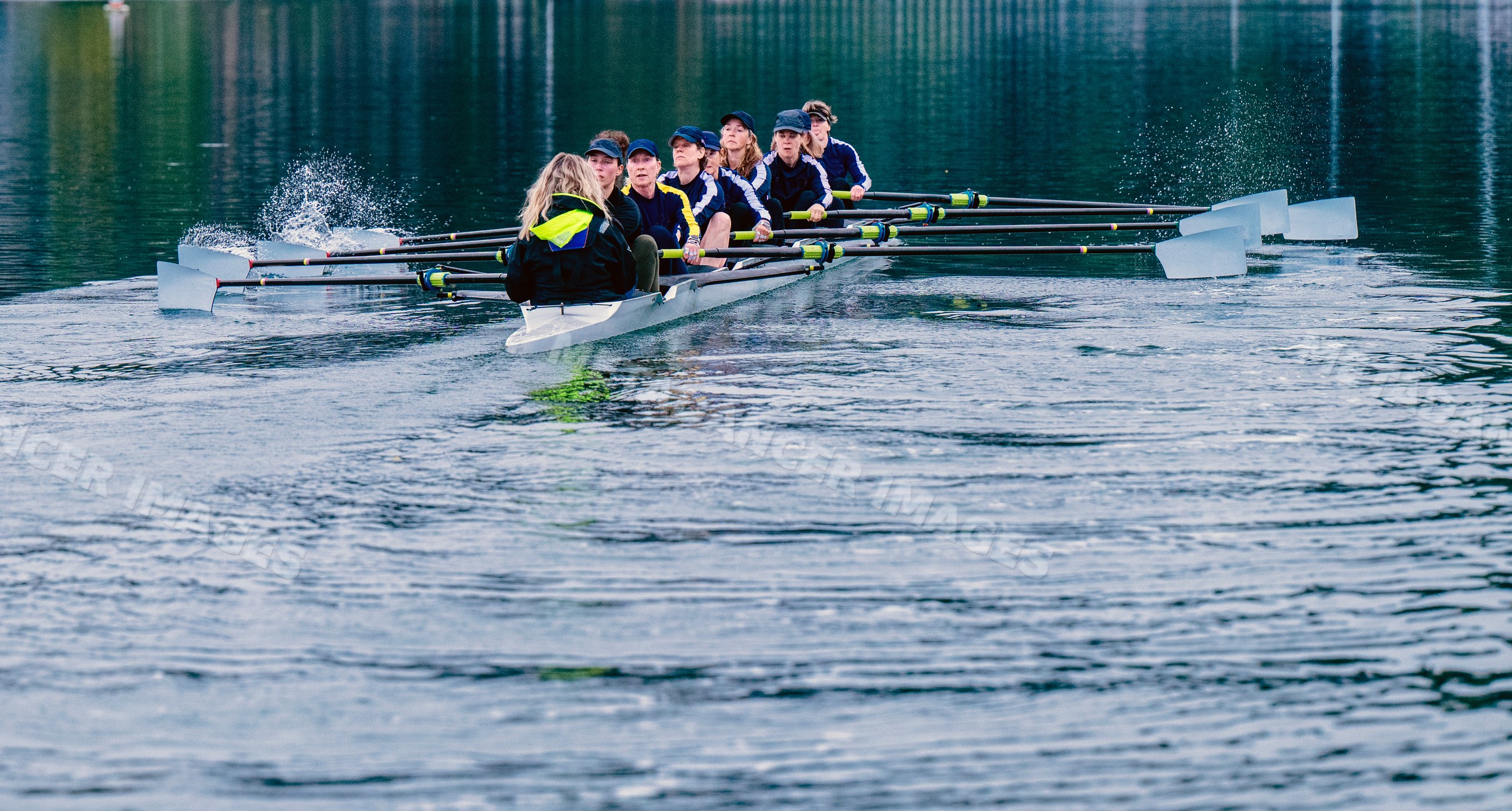 An eight-white person rowing team rows together in calm water