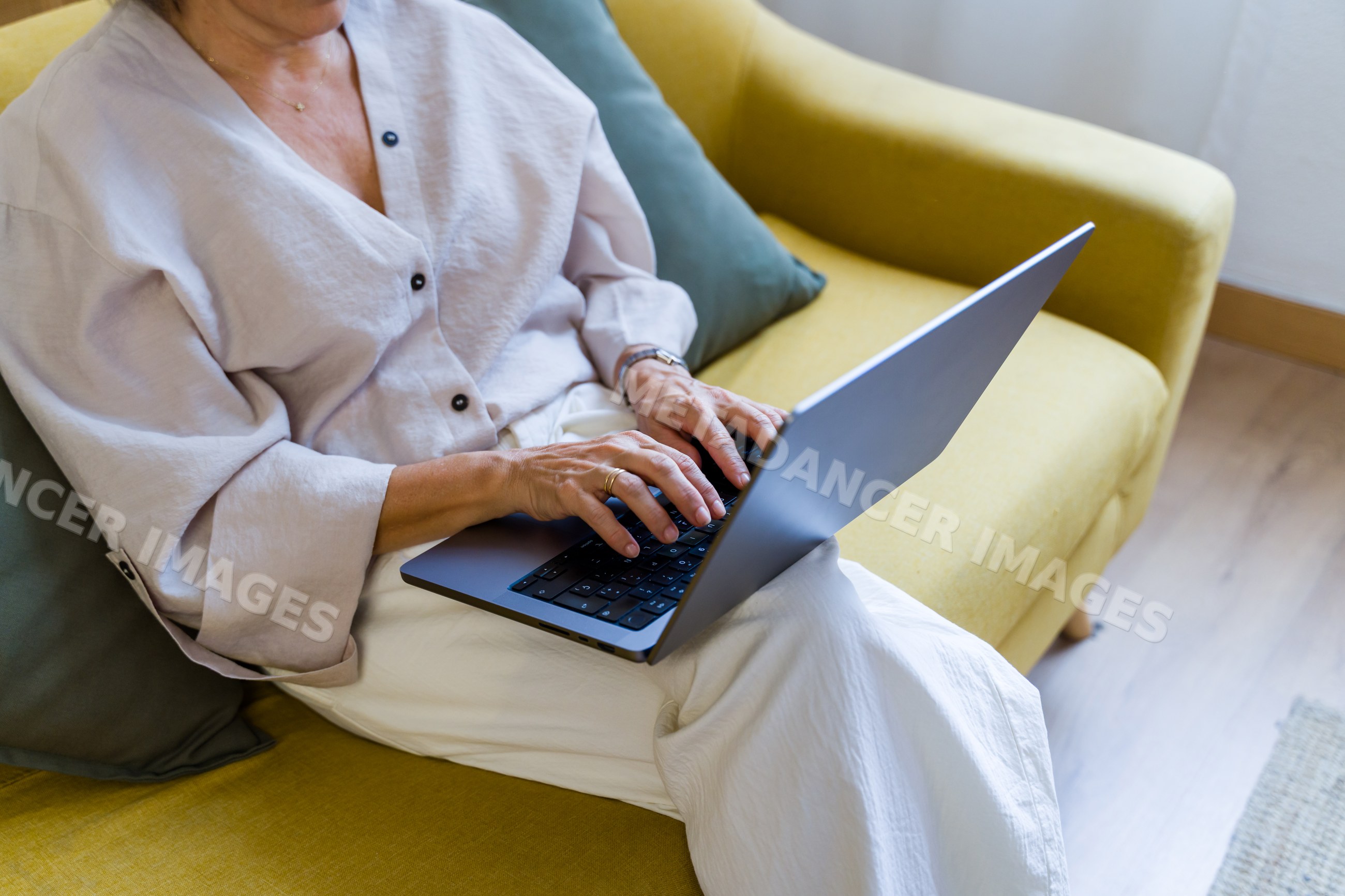 White woman typing on laptop on yellow couch indoors