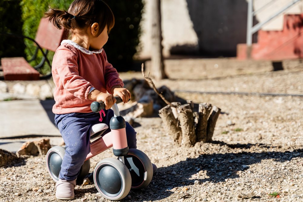Toddler white girl riding balance bike outdoors in a park