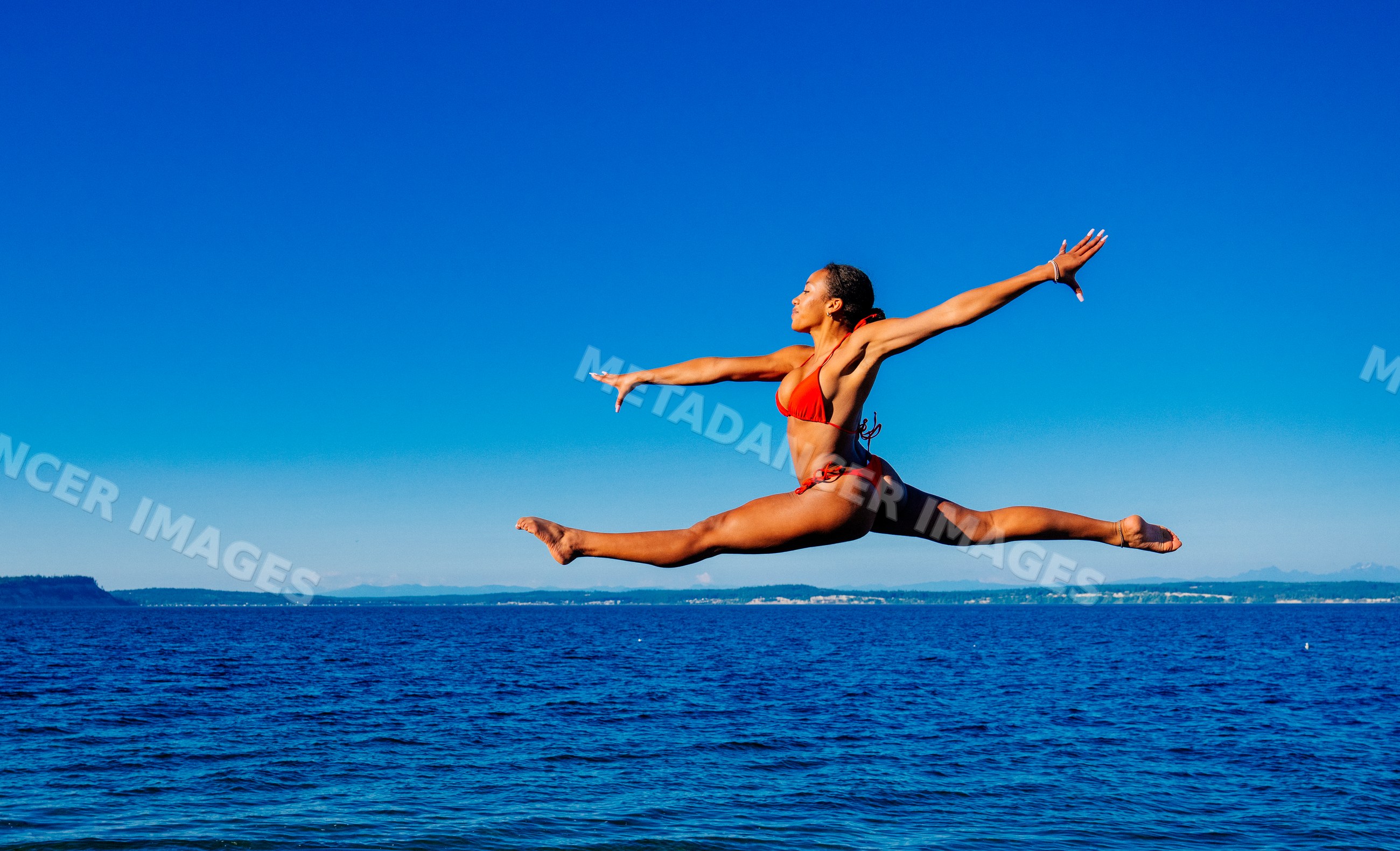 A woman jumps in a red bikini over the ocean on a clear sunny day