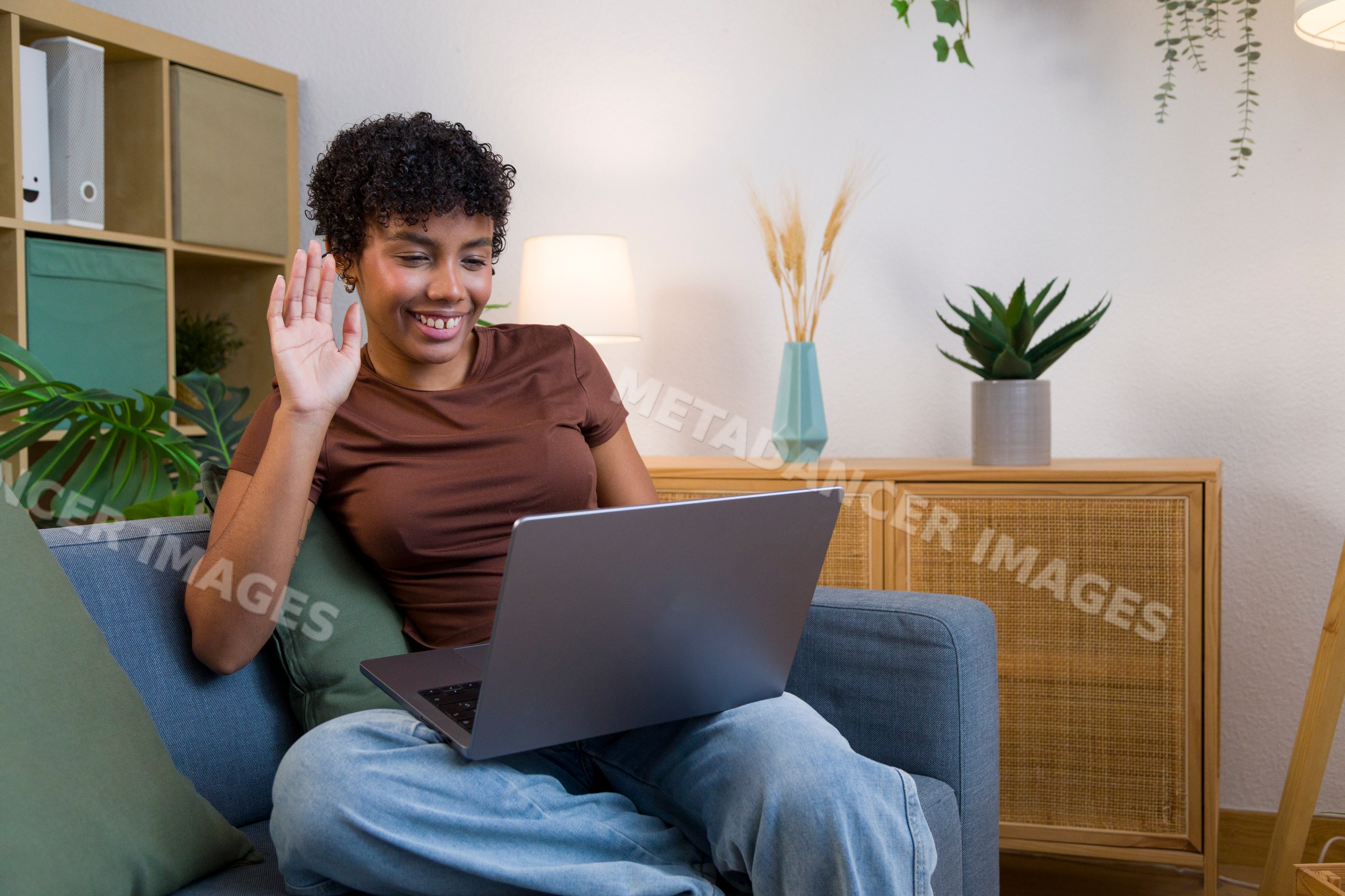 African American woman waving during video call at home on sofa