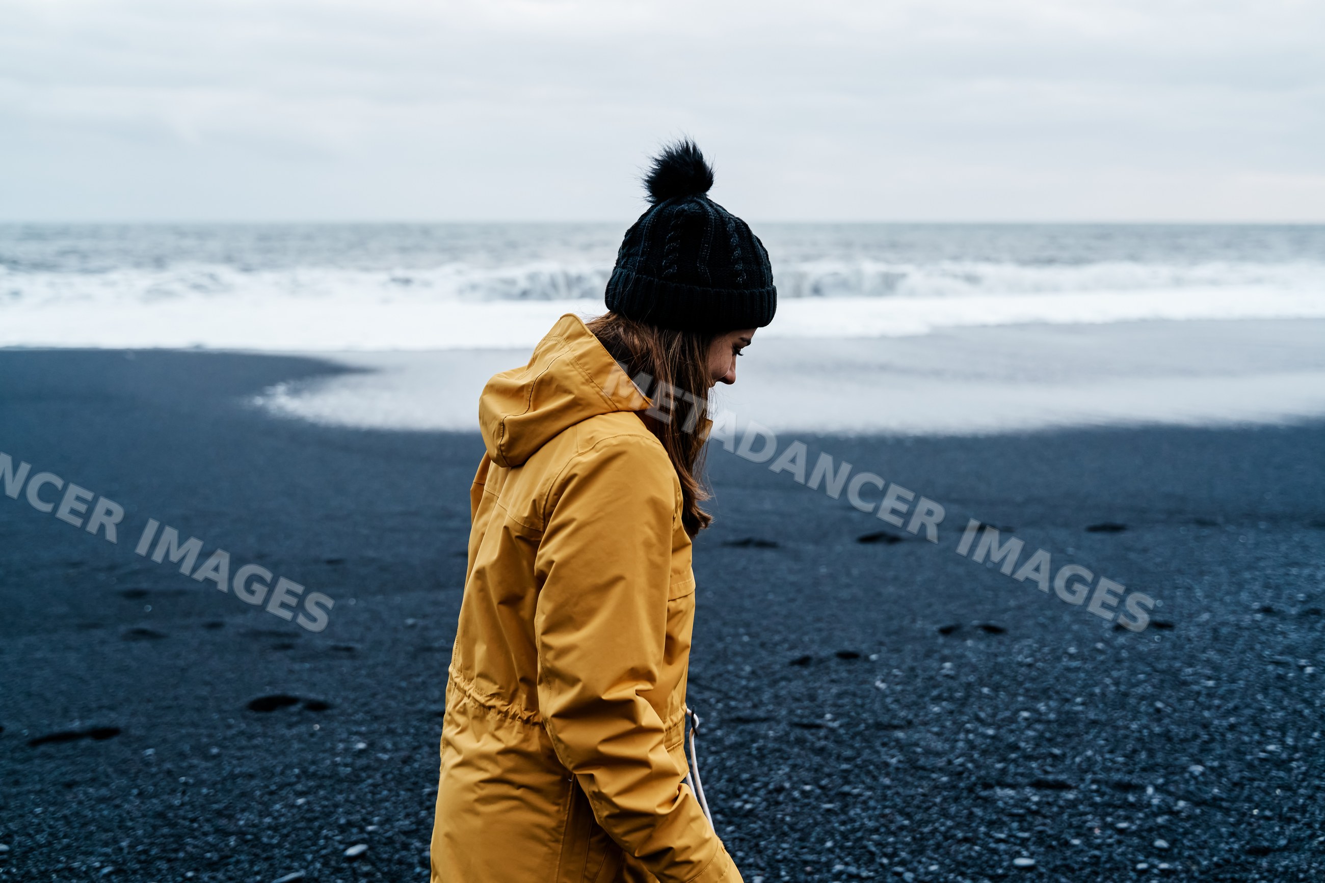 A white woman walks along a black sand beach near the ocean in Iceland