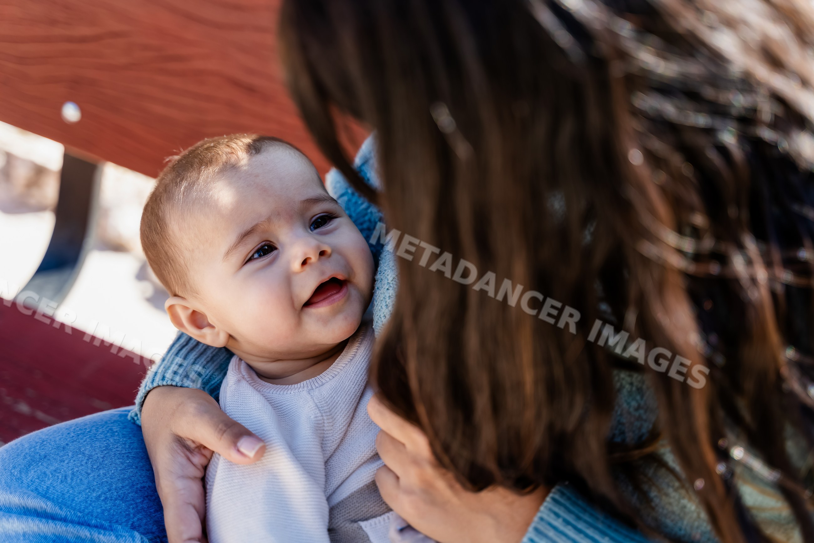 Baby smiling in white woman's arms on outdoor bench