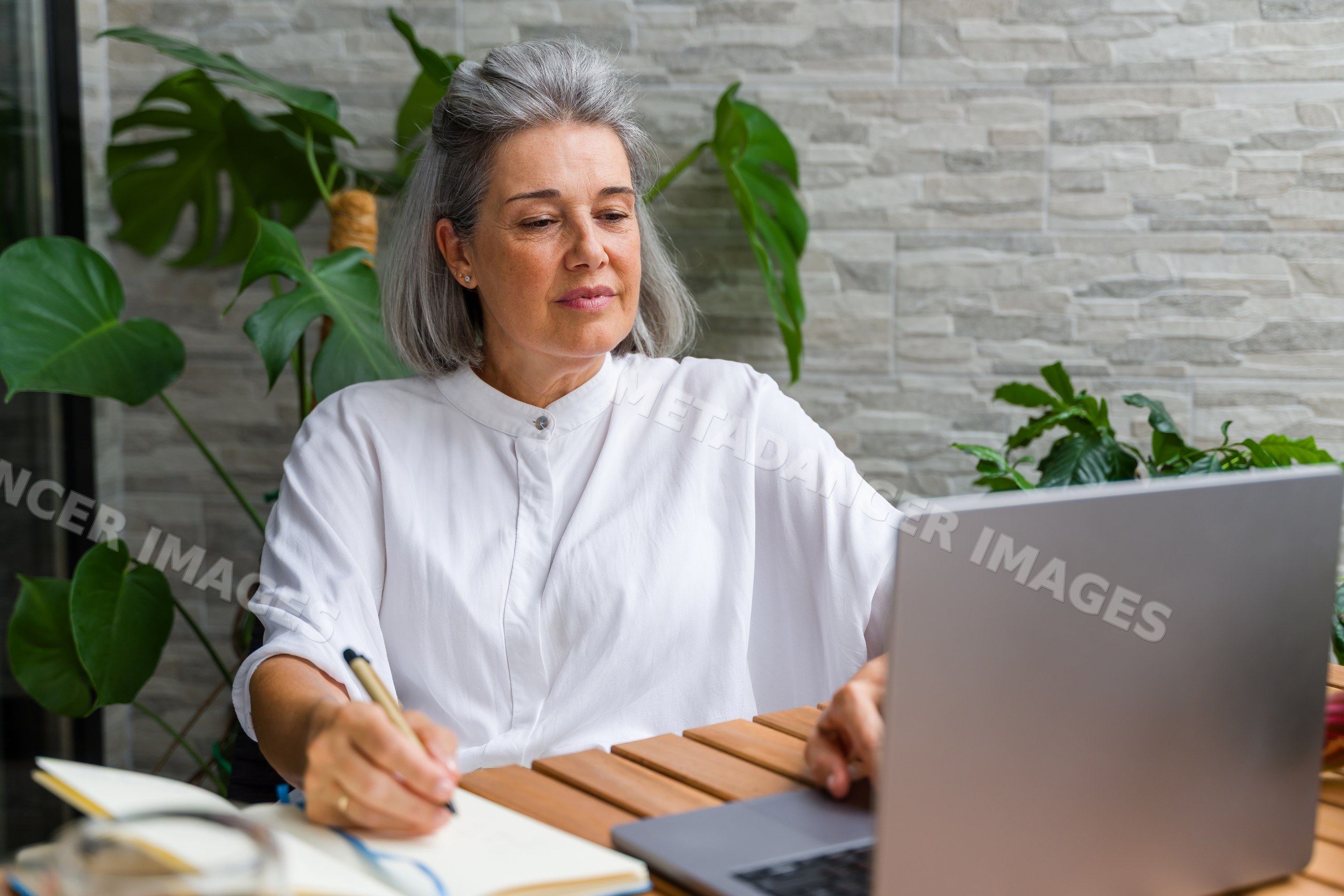Mature white woman writing and working on laptop