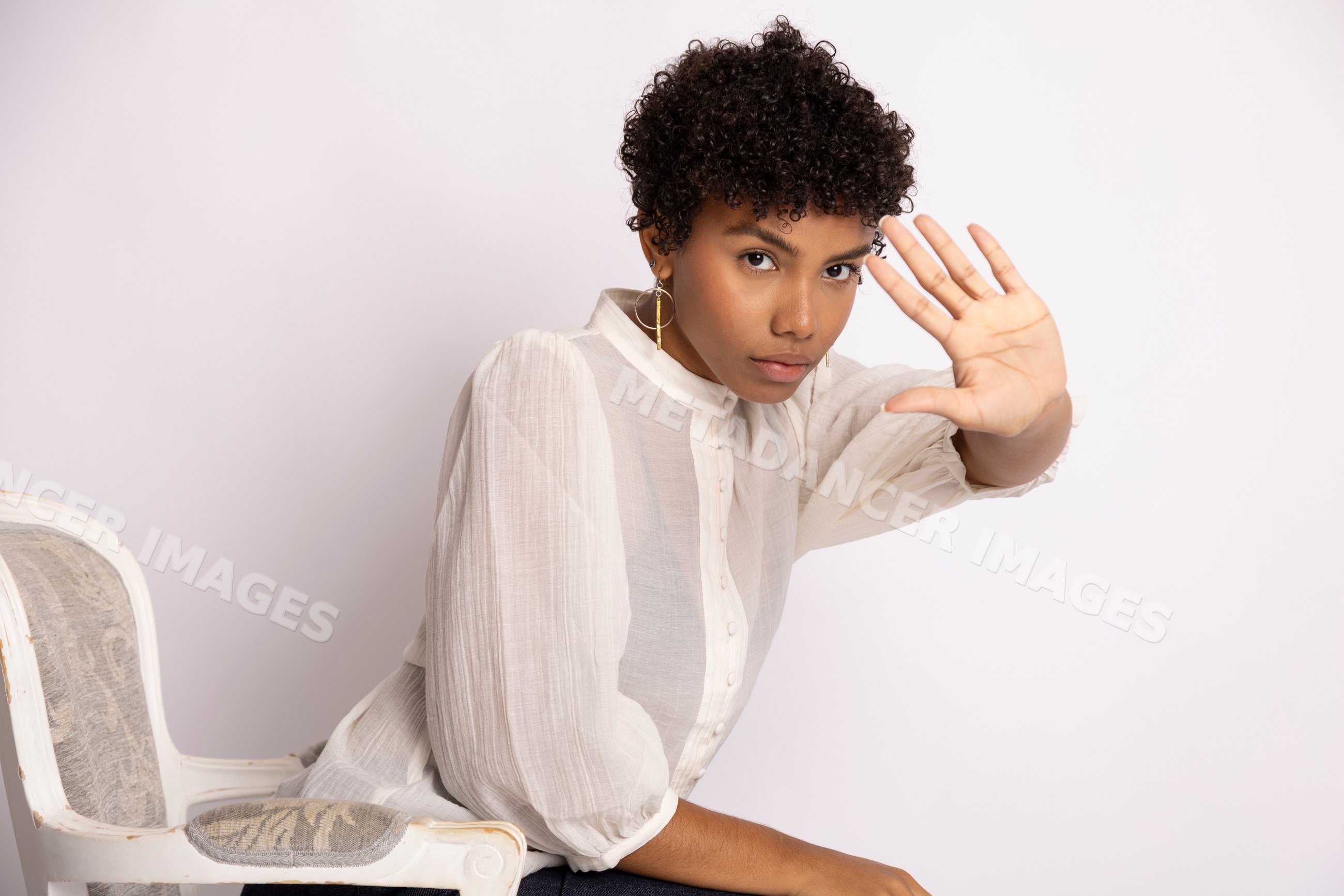 Young Hispanic woman with curly hair raising hand in a studio