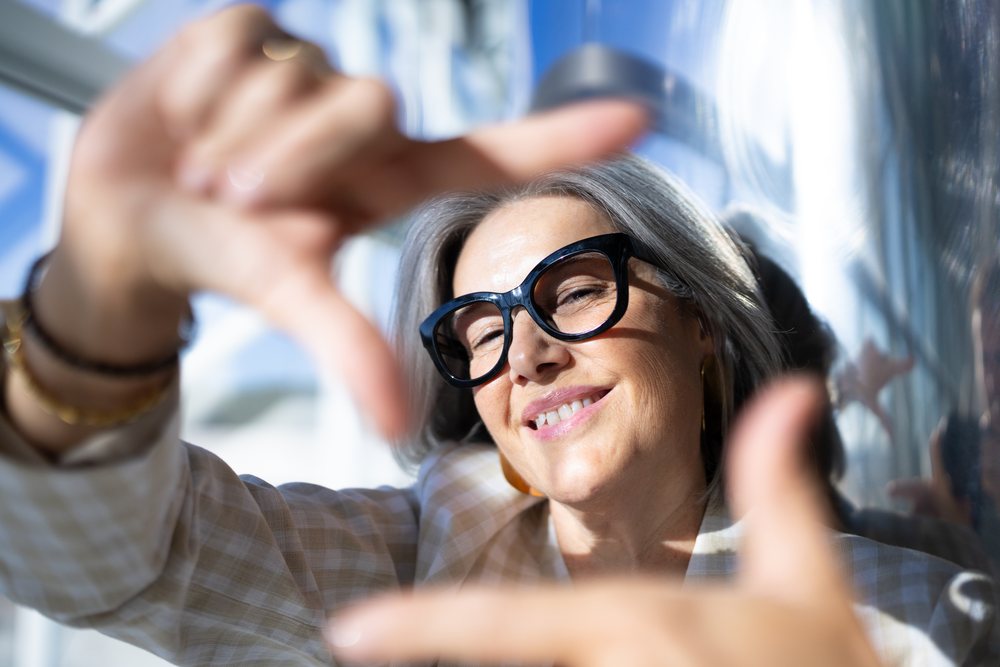 White woman with gray hair framing face with hands and smiling