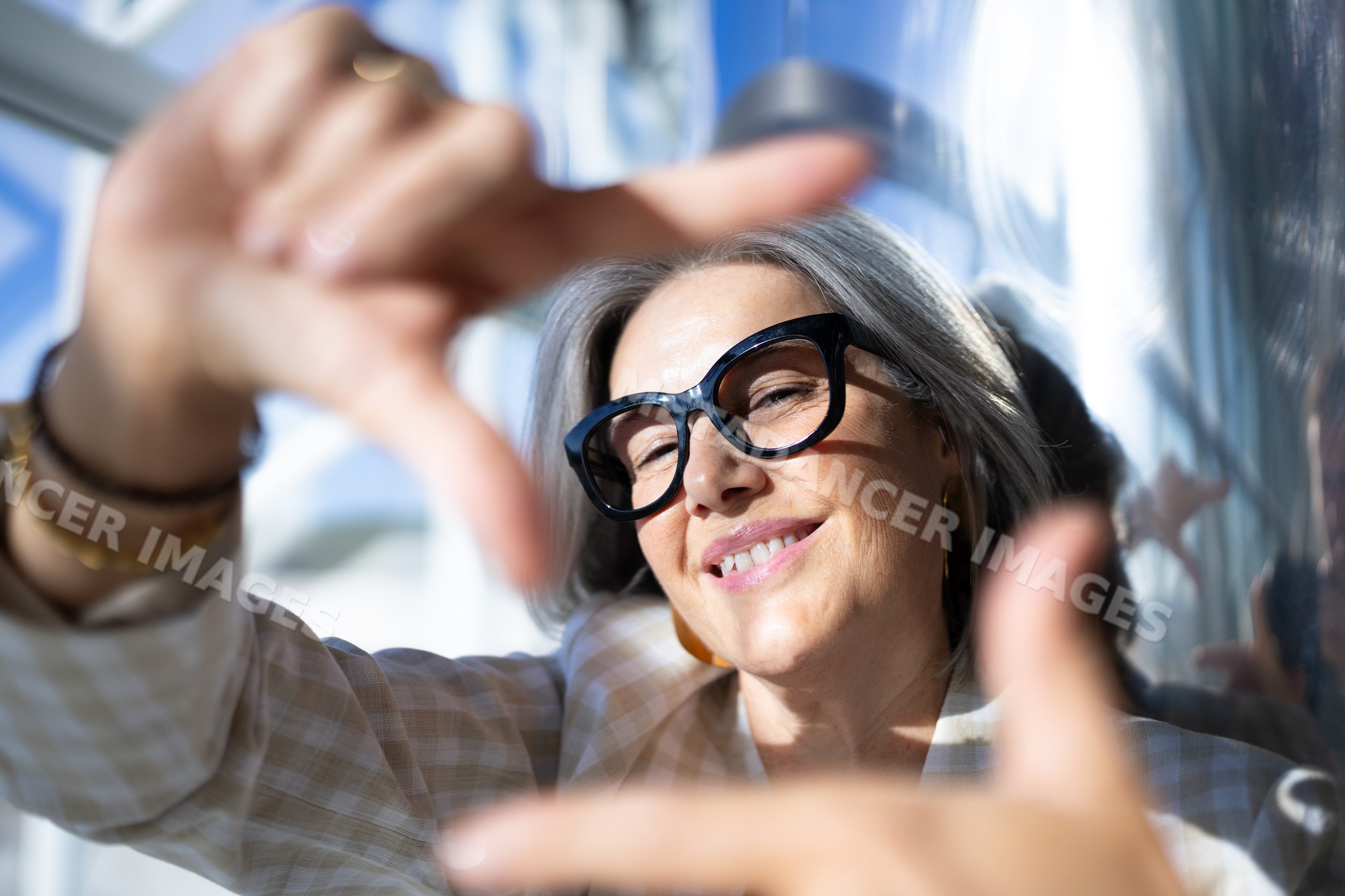 White woman with gray hair framing face with hands and smiling
