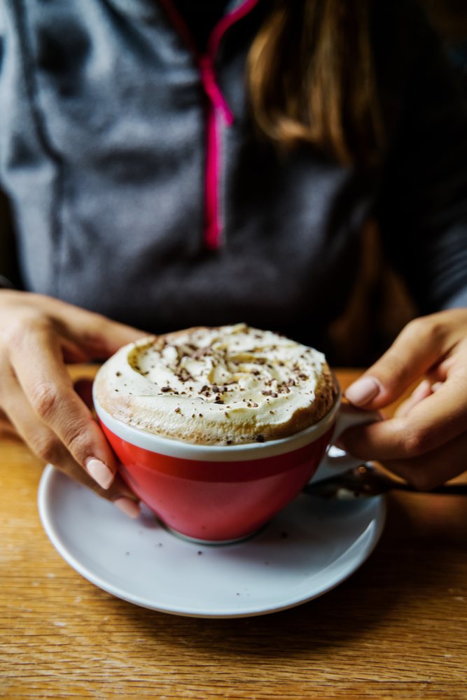 A white woman holds a cup of hot chocolate with whipped cream