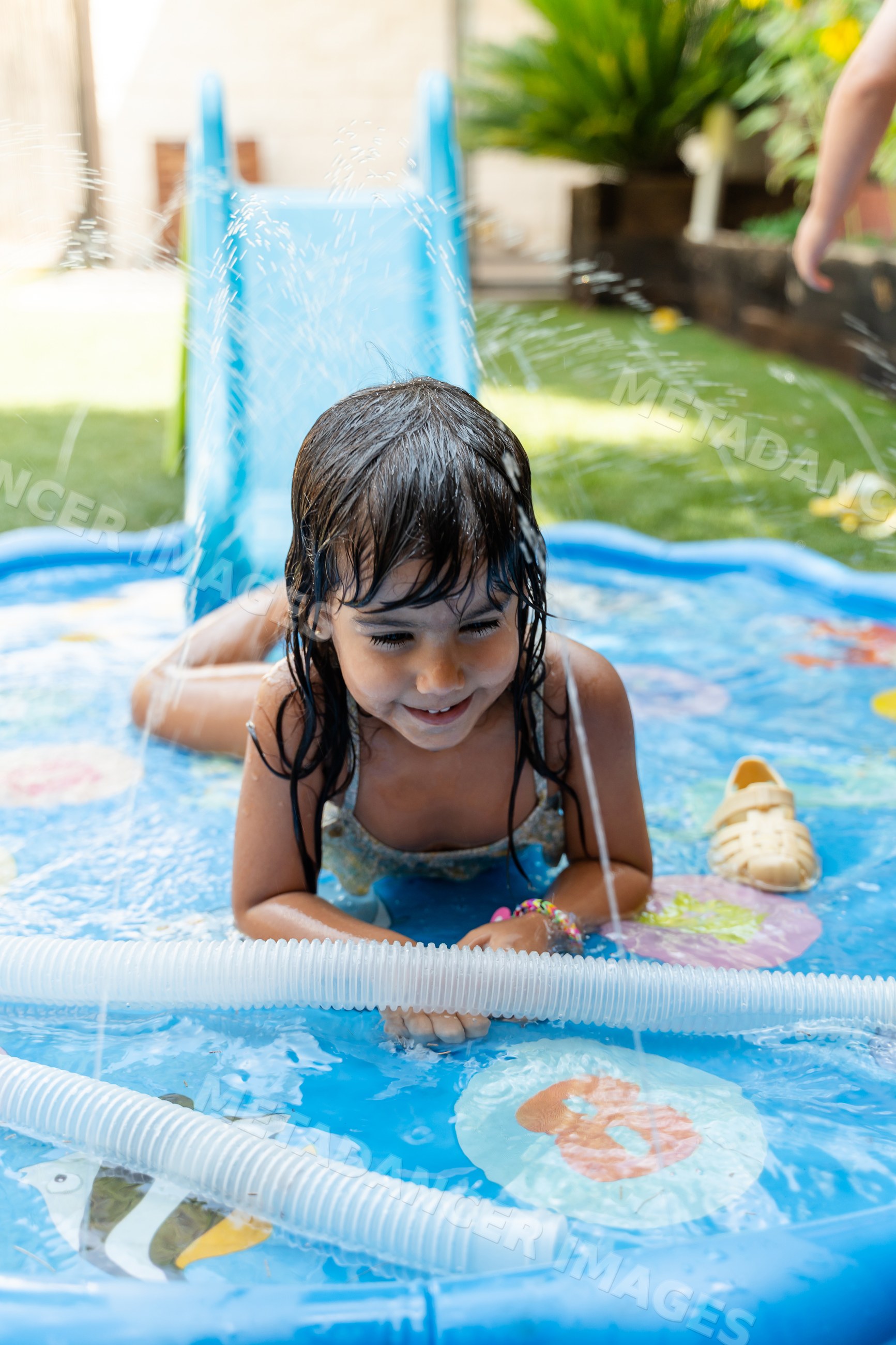A young white girl enjoys playing in an inflatable pool on a sunny day