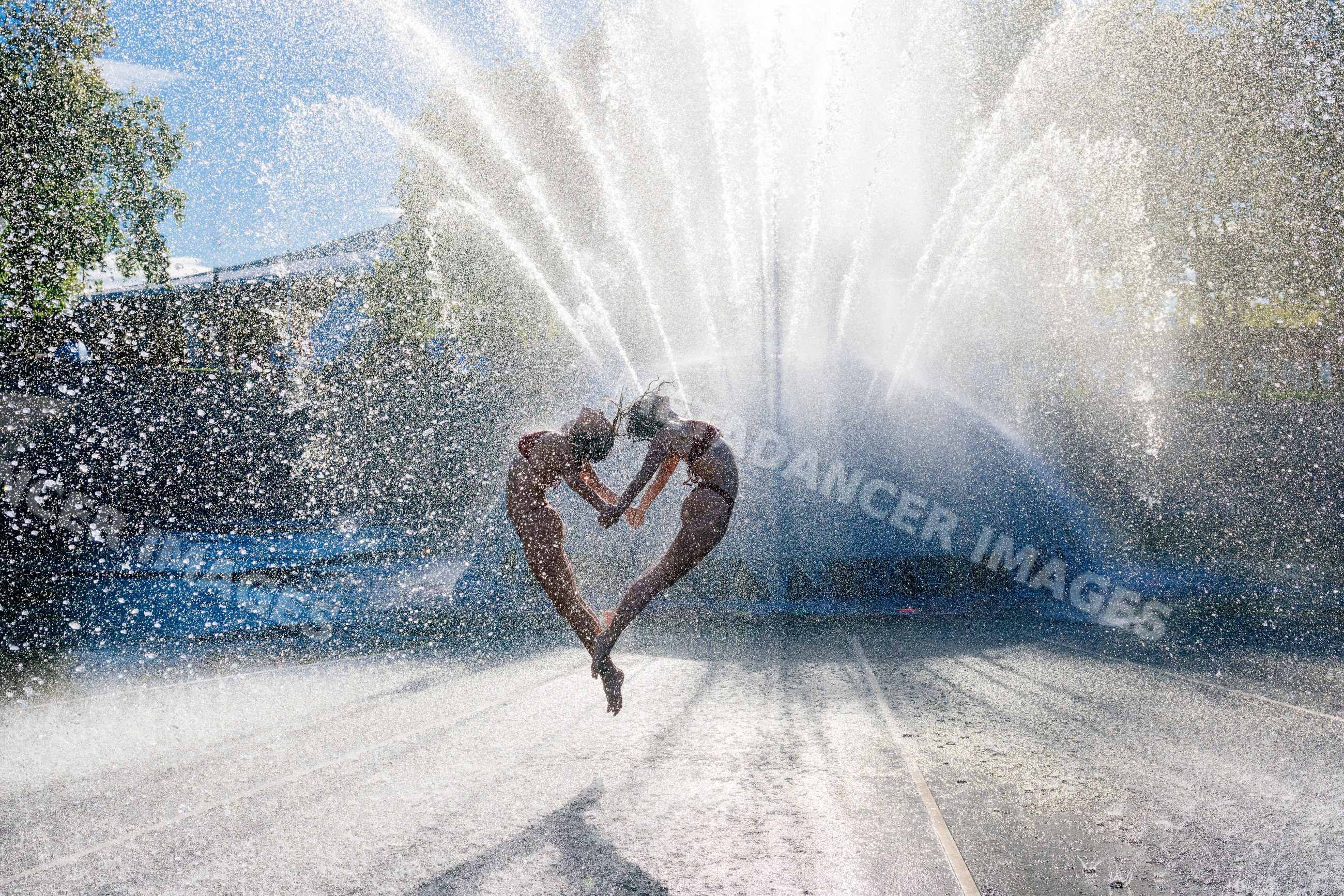 Two individuals performing synchronized acrobatic yoga jump by water