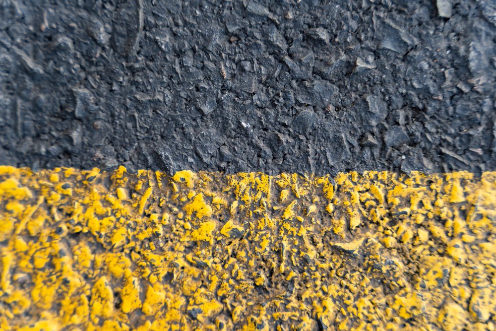 Close-up of rough asphalt pavement with worn yellow line