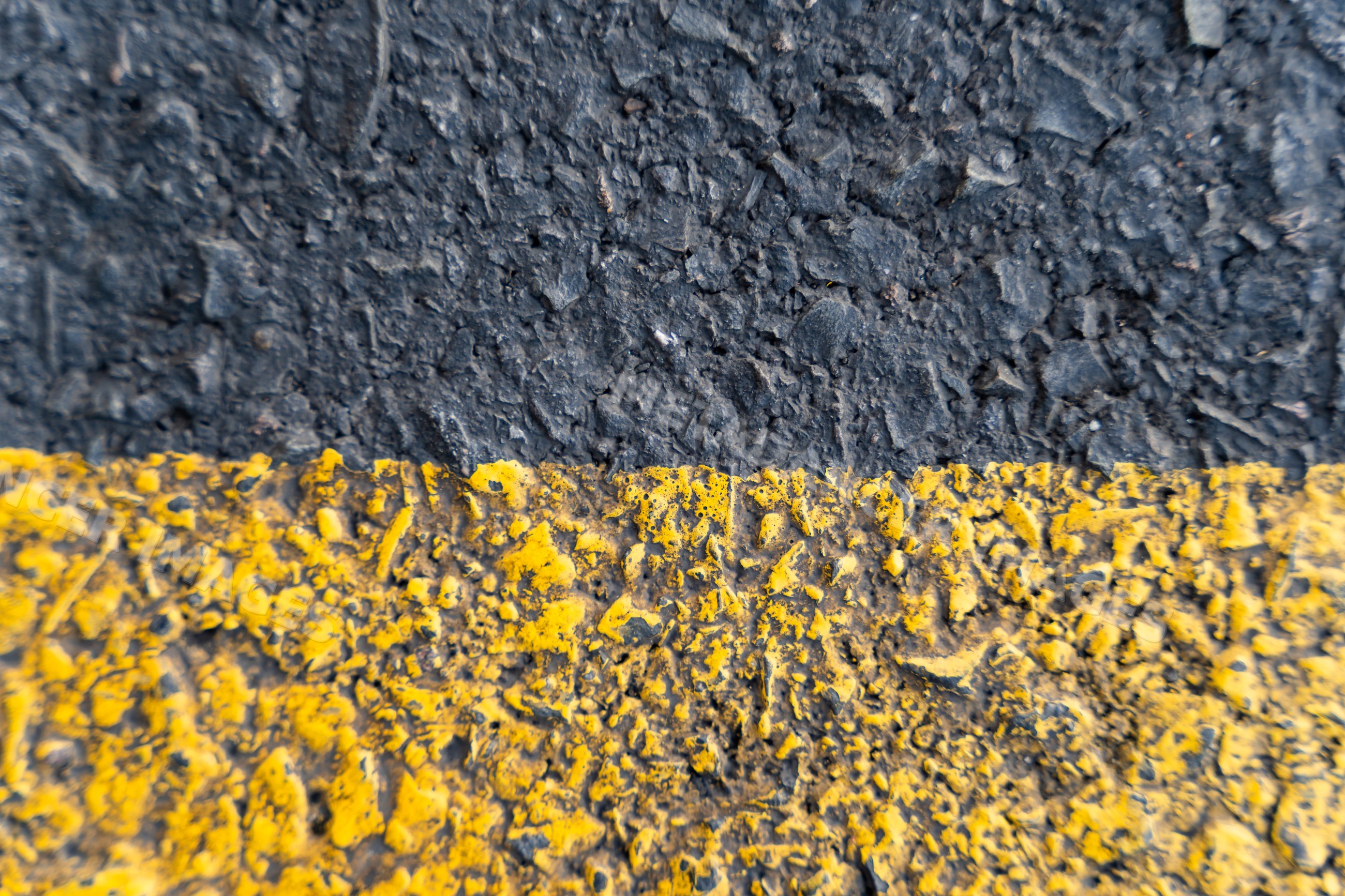 Close-up of rough asphalt pavement with worn yellow line