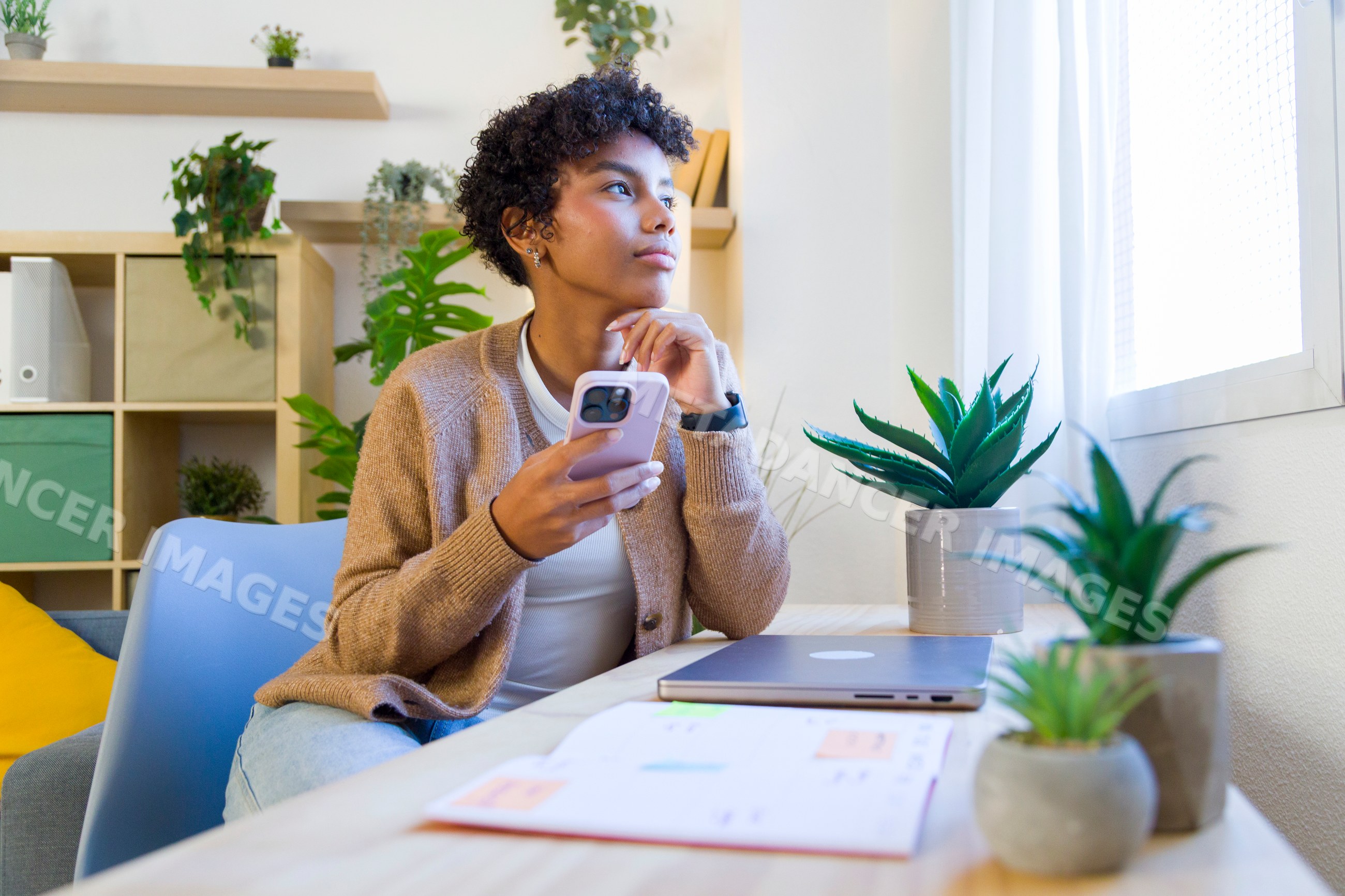 African American woman holding smartphone looking out window