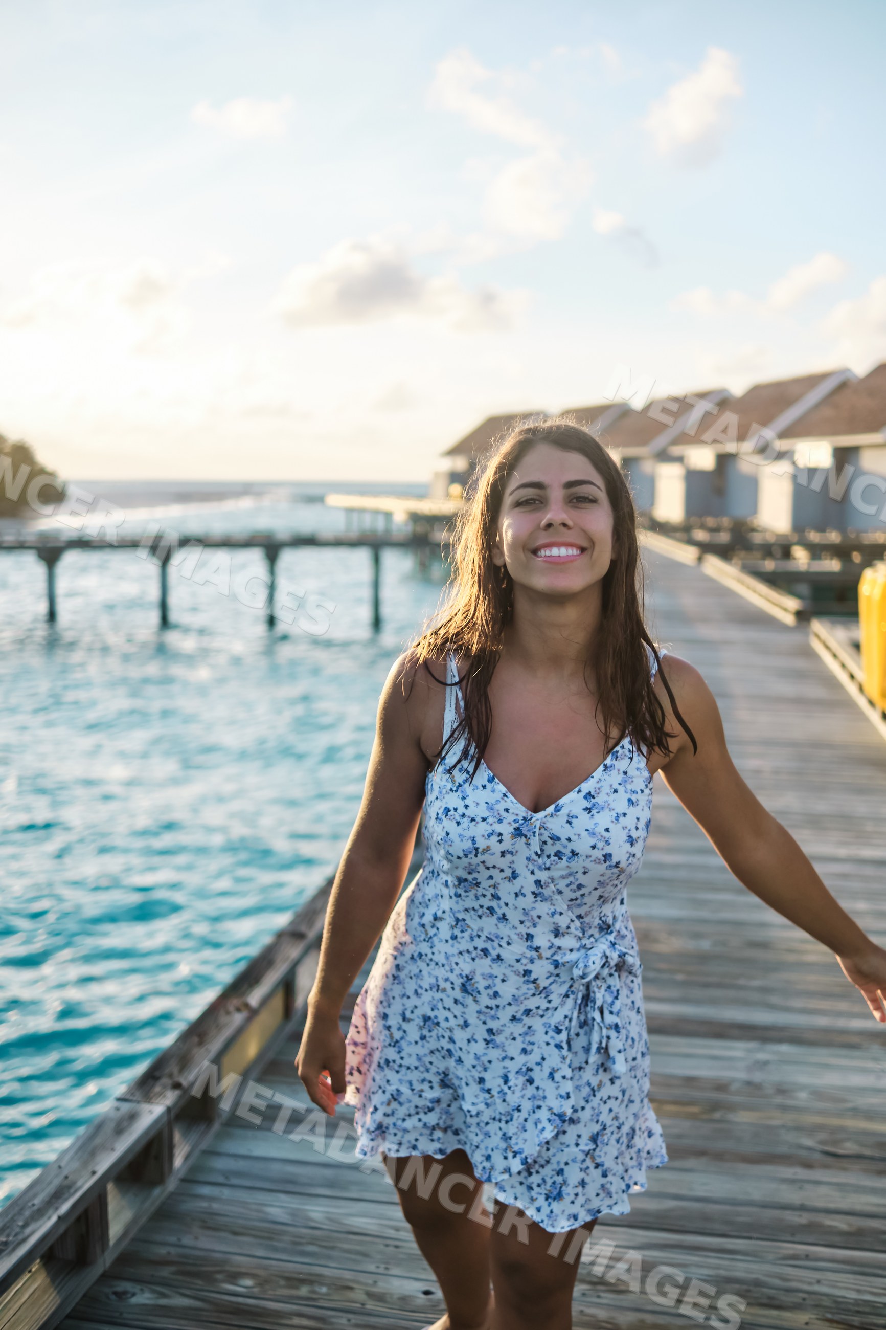 A smiling white woman walks on a wooden pier at a resort