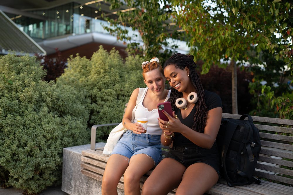 Two friends sitting on a bench looking at a smartphone in Santiago