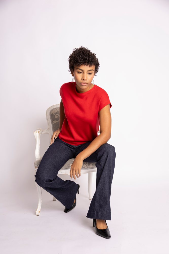 Young Hispanic woman in red short-sleeve top and jeans sitting