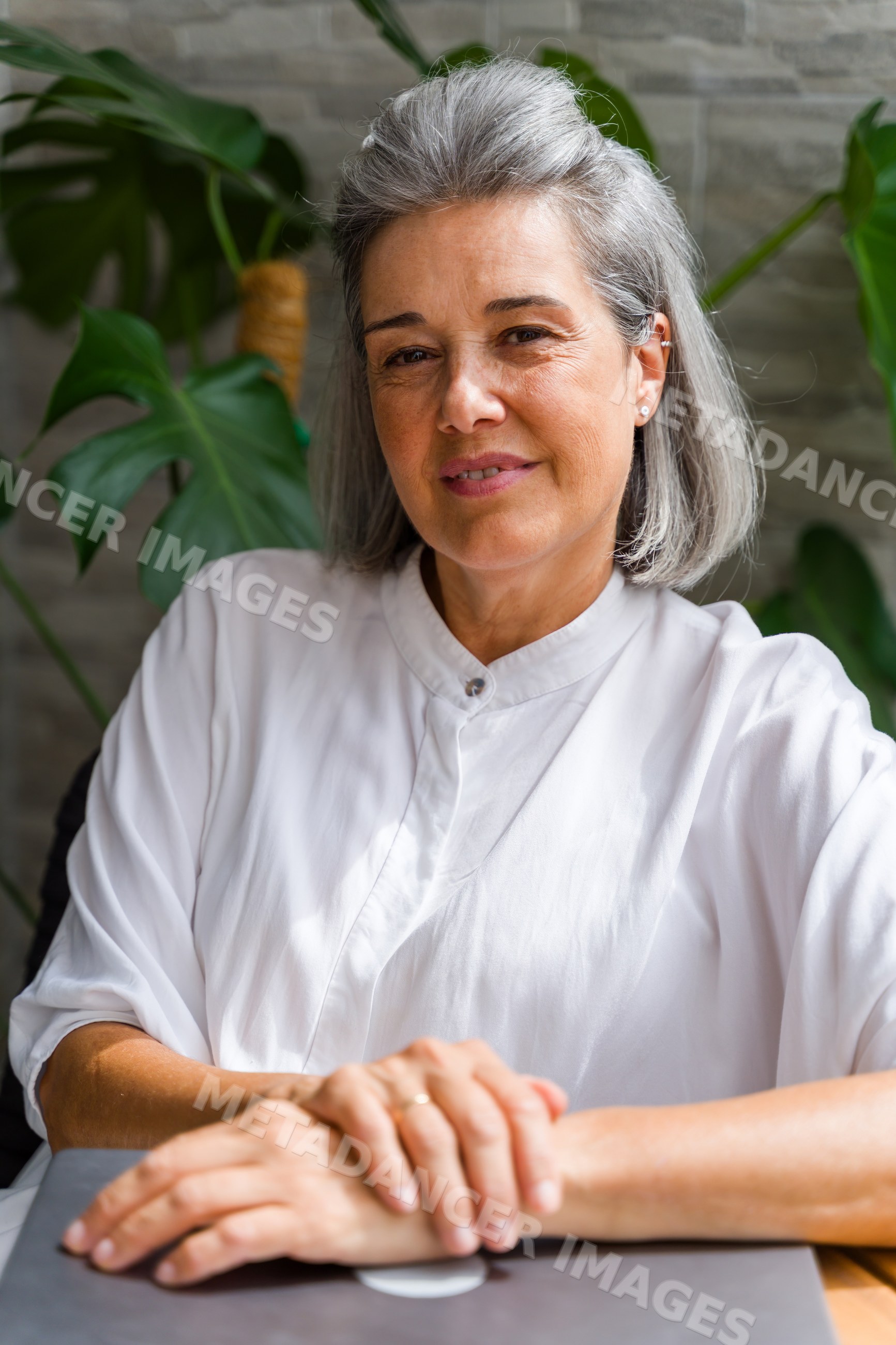 Middle-aged white woman sitting indoors with folded hands and plants