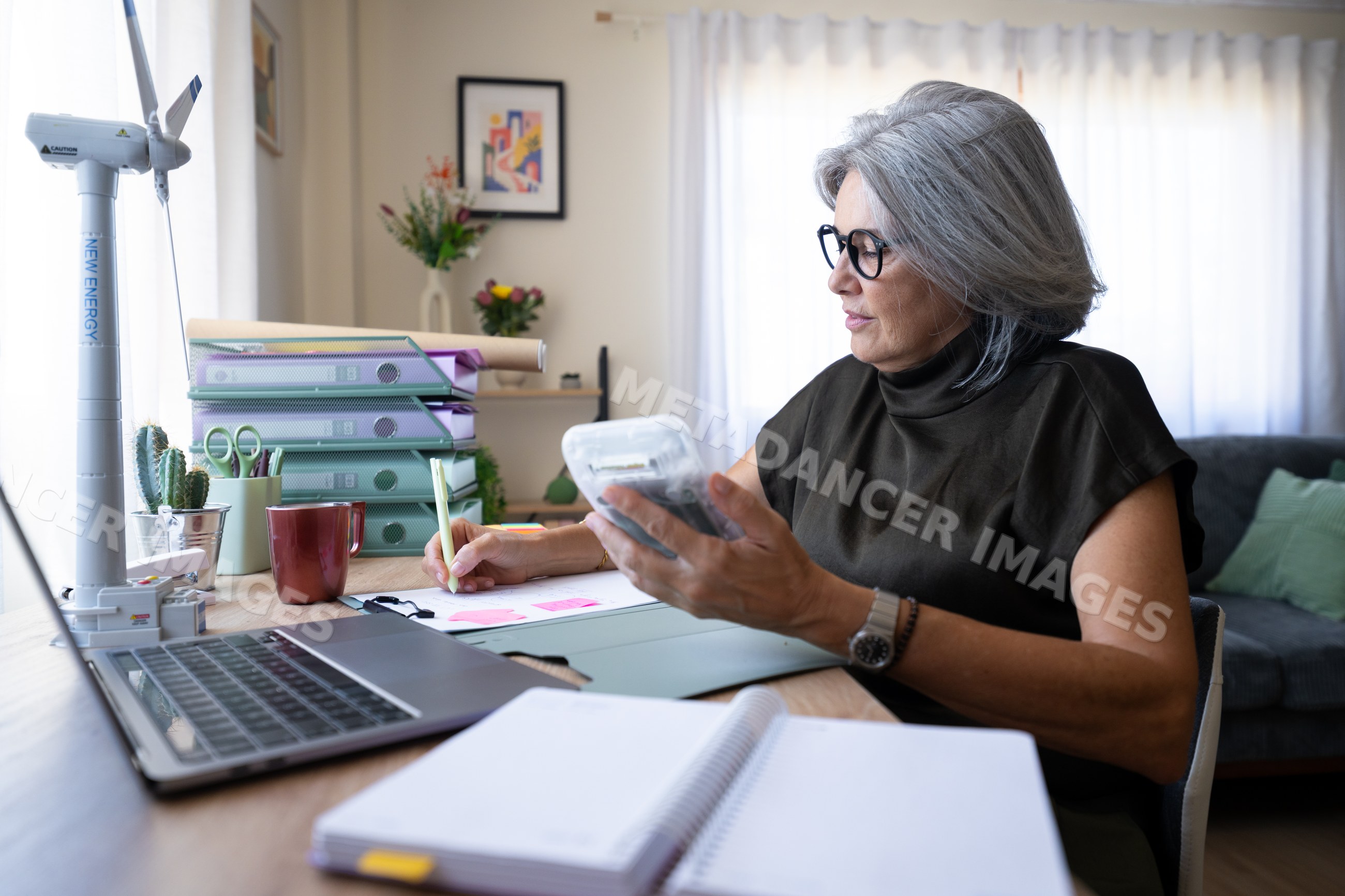 White woman working at desk with calculator and laptop in home office