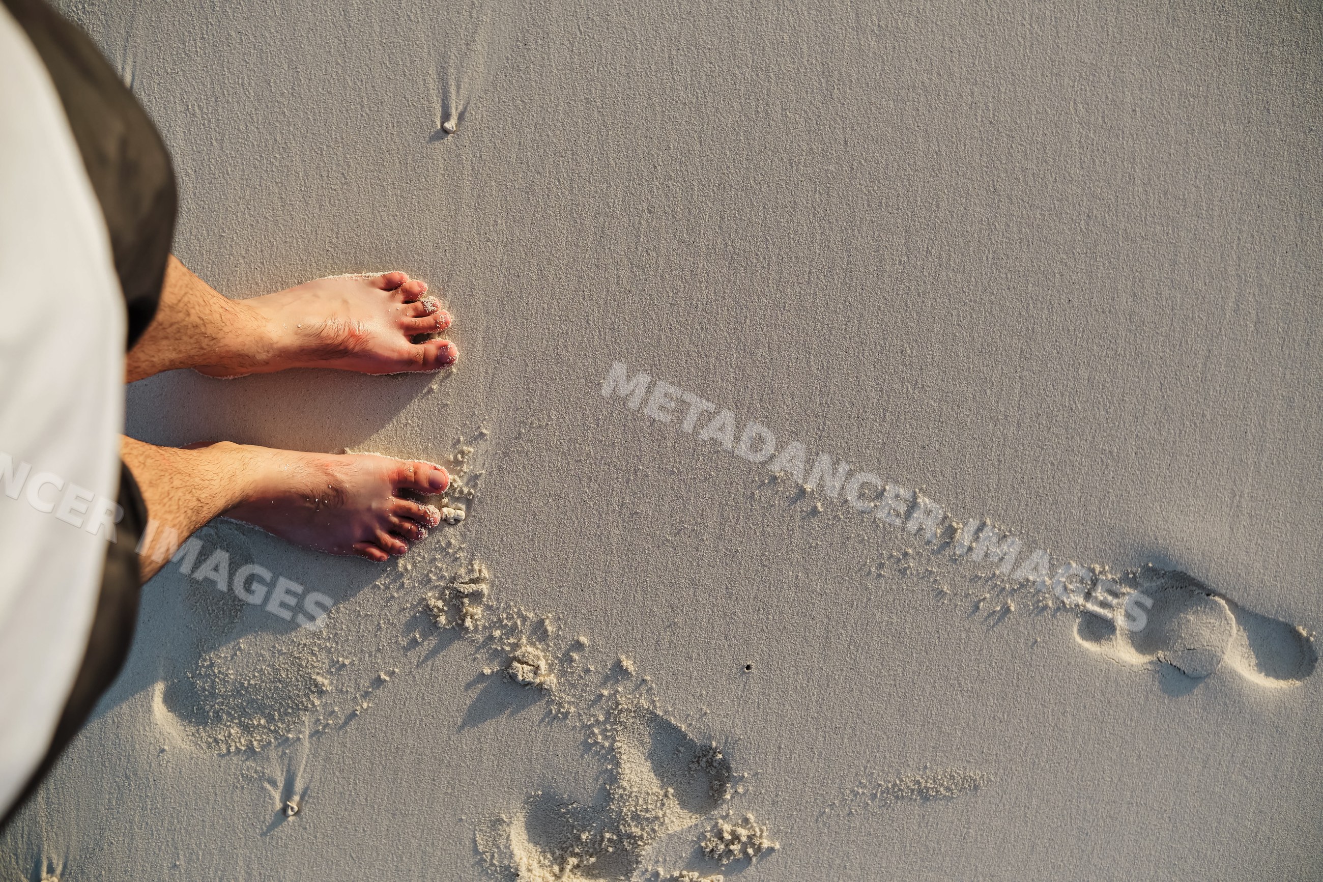 Person standing barefoot on soft sand with footprints on a beach