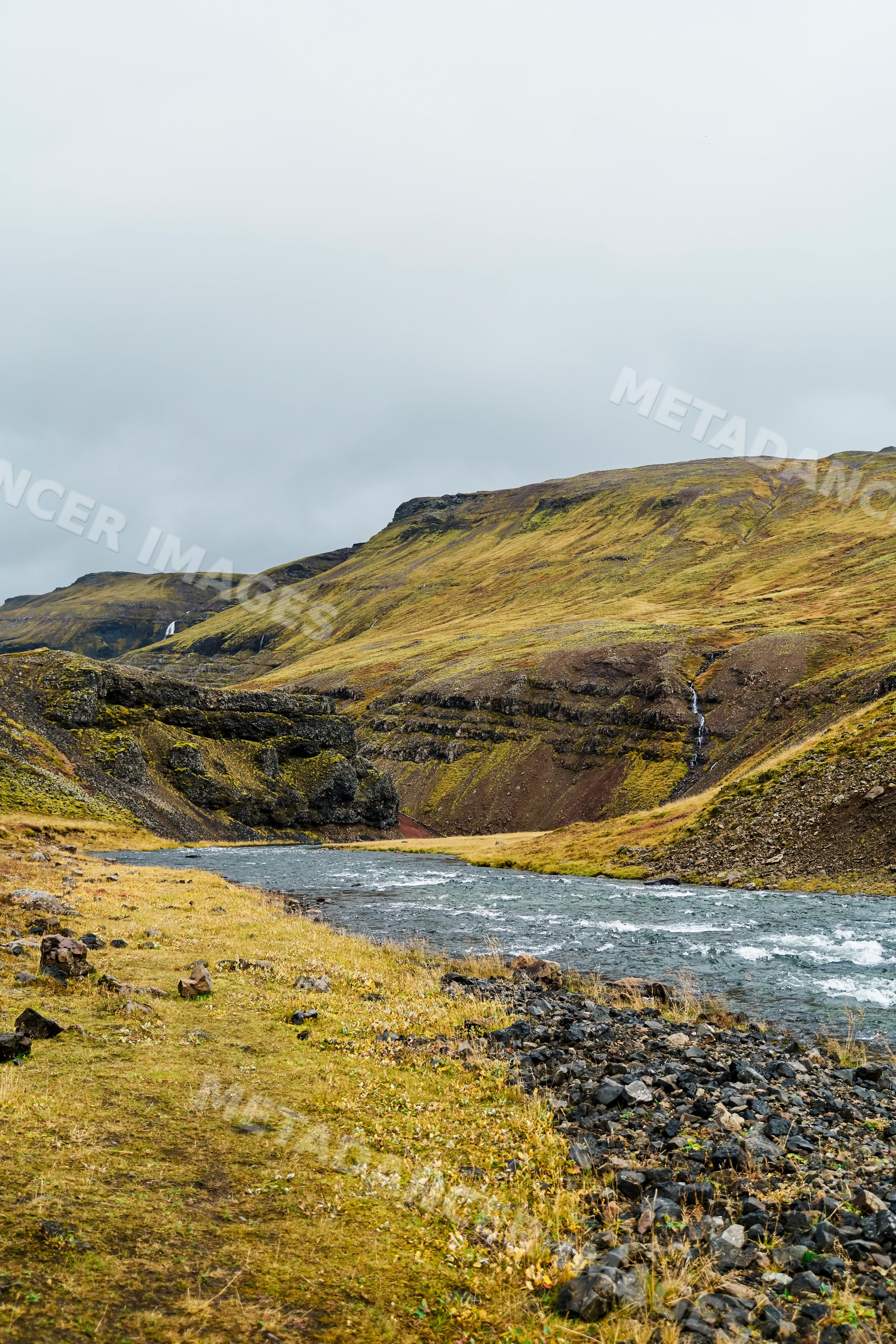 A river flows through hills and waterfalls in a rocky Iceland valley