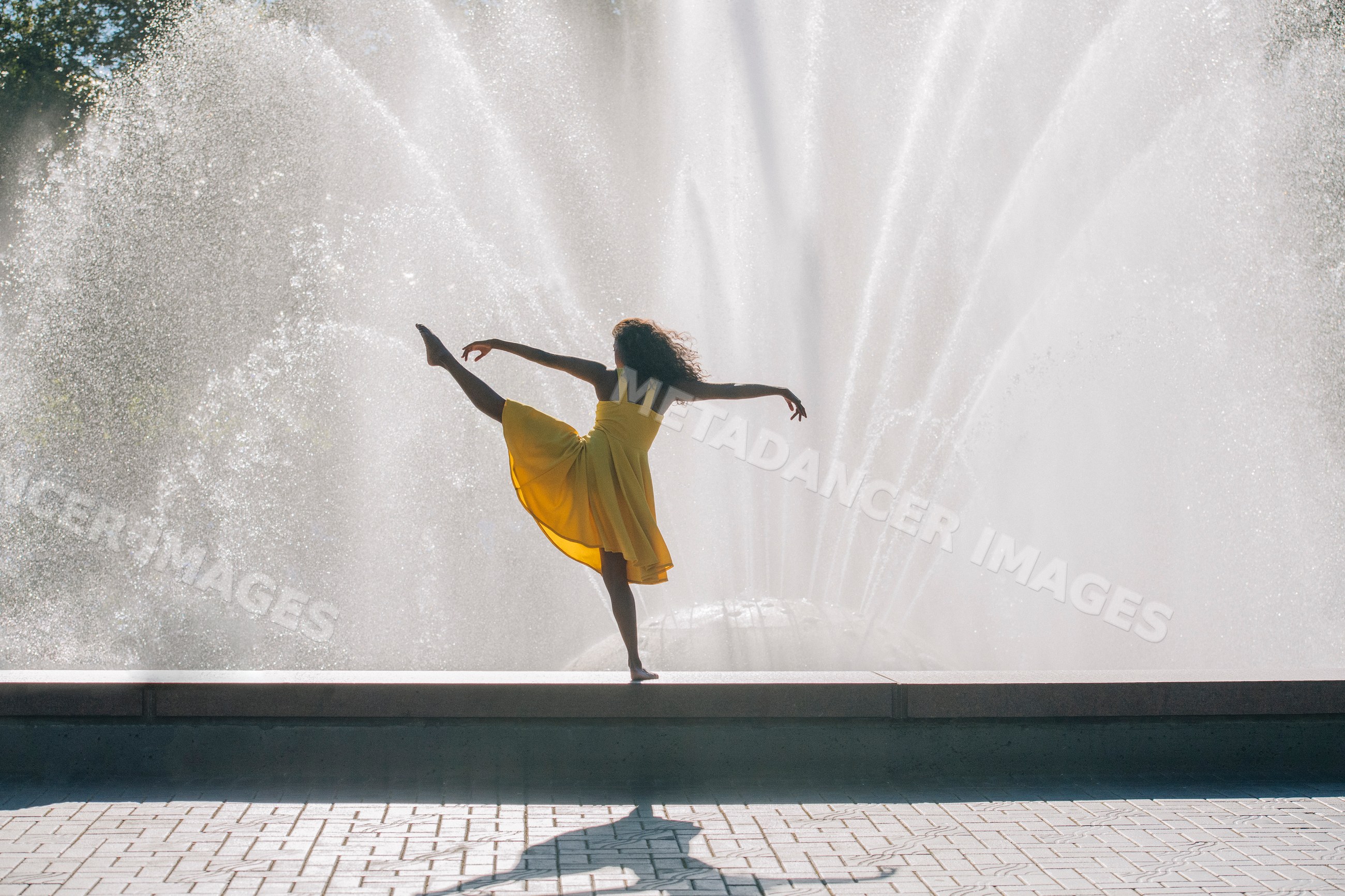 South Asian dancer performing pose in yellow dress by water fountain