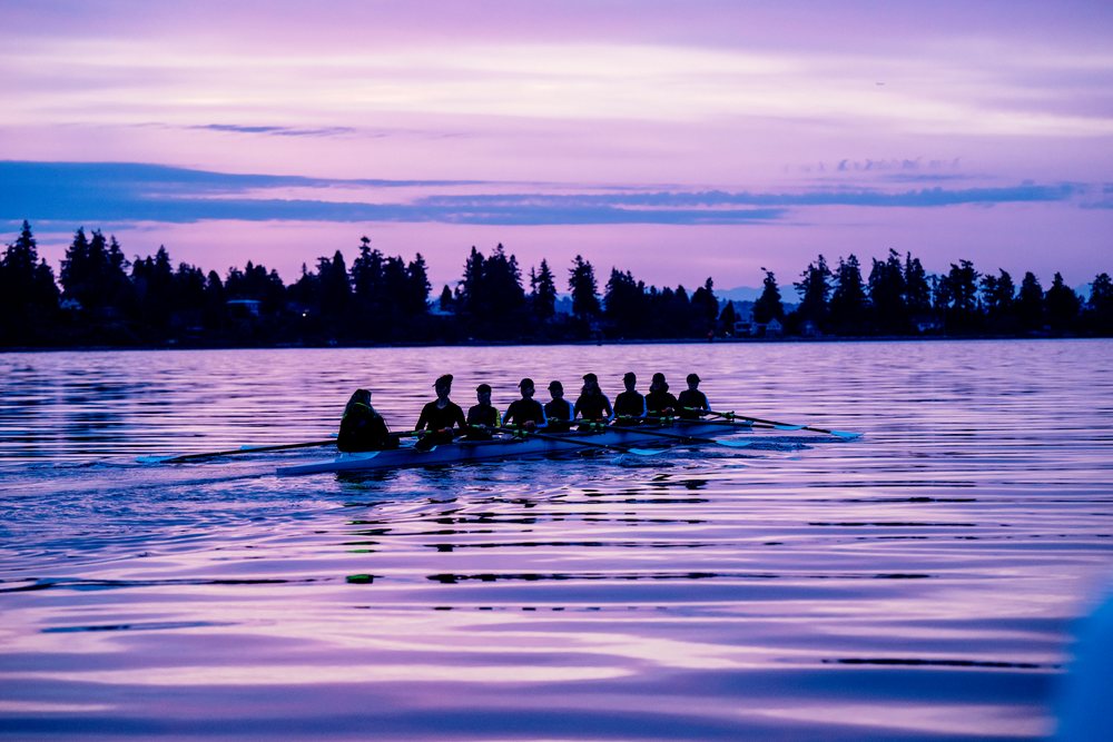 A rowing team trains together on calm lake water at sunset