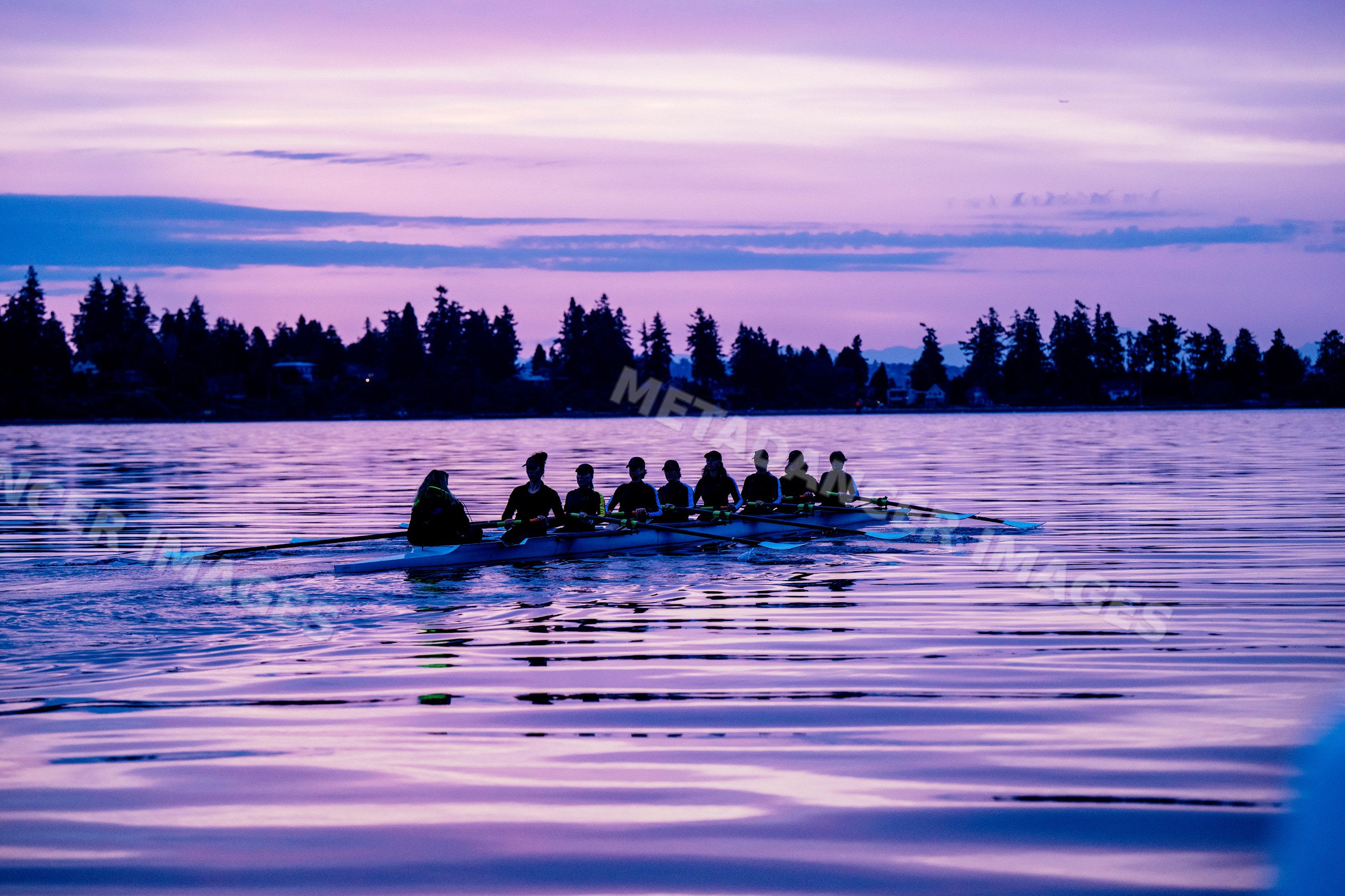 A rowing team trains together on calm lake water at sunset