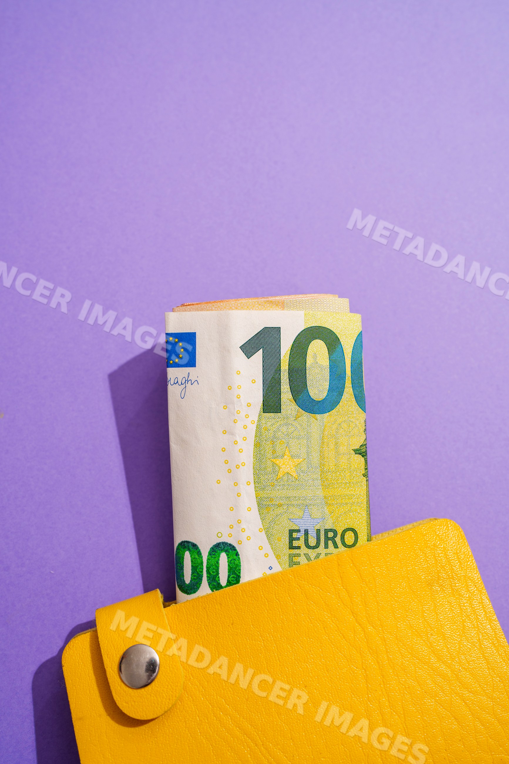 Rolled 100 euro banknote in yellow wallet on purple background